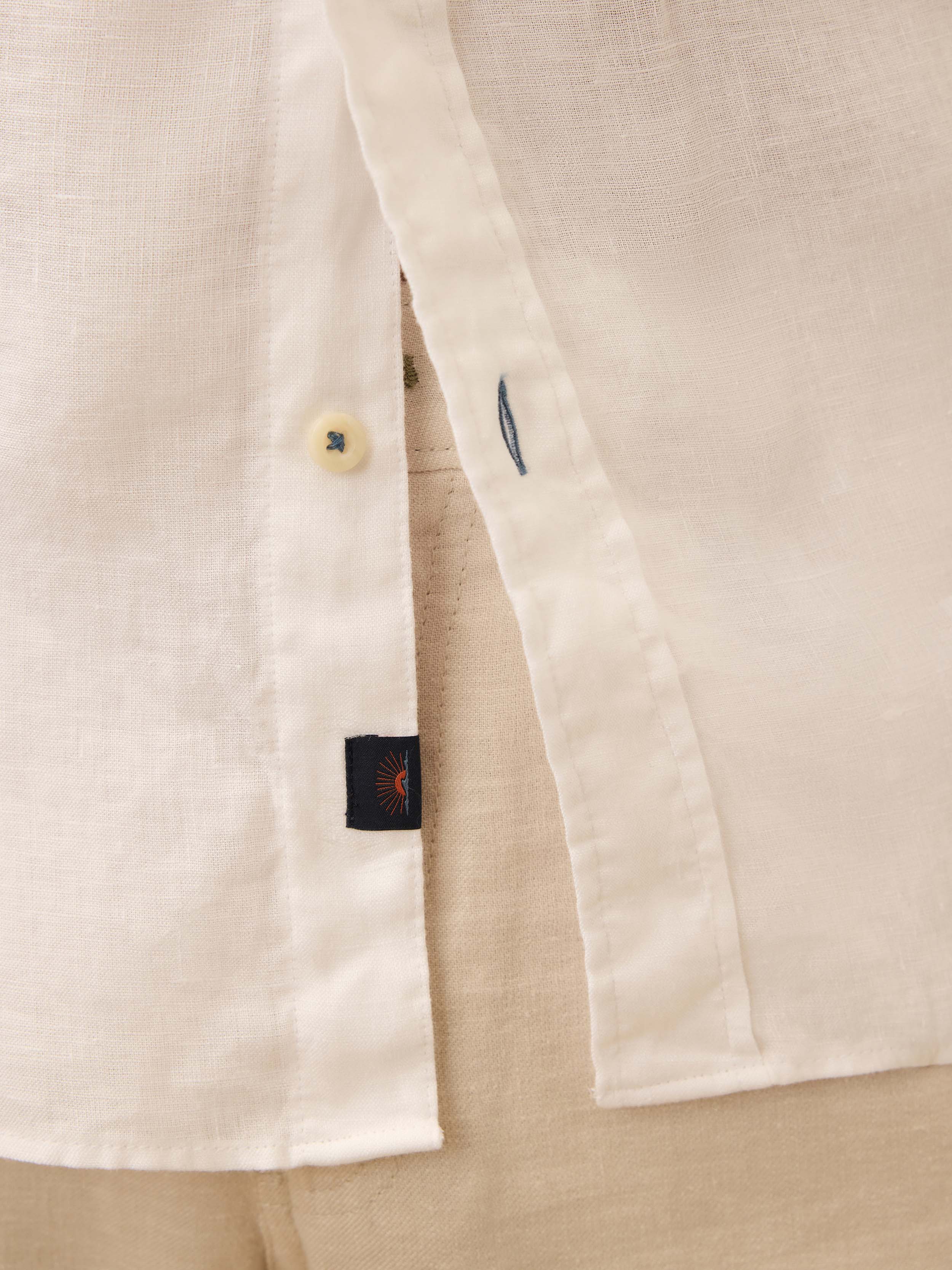 Close-up of a white linen shirt with a Faherty brand logo and button details.