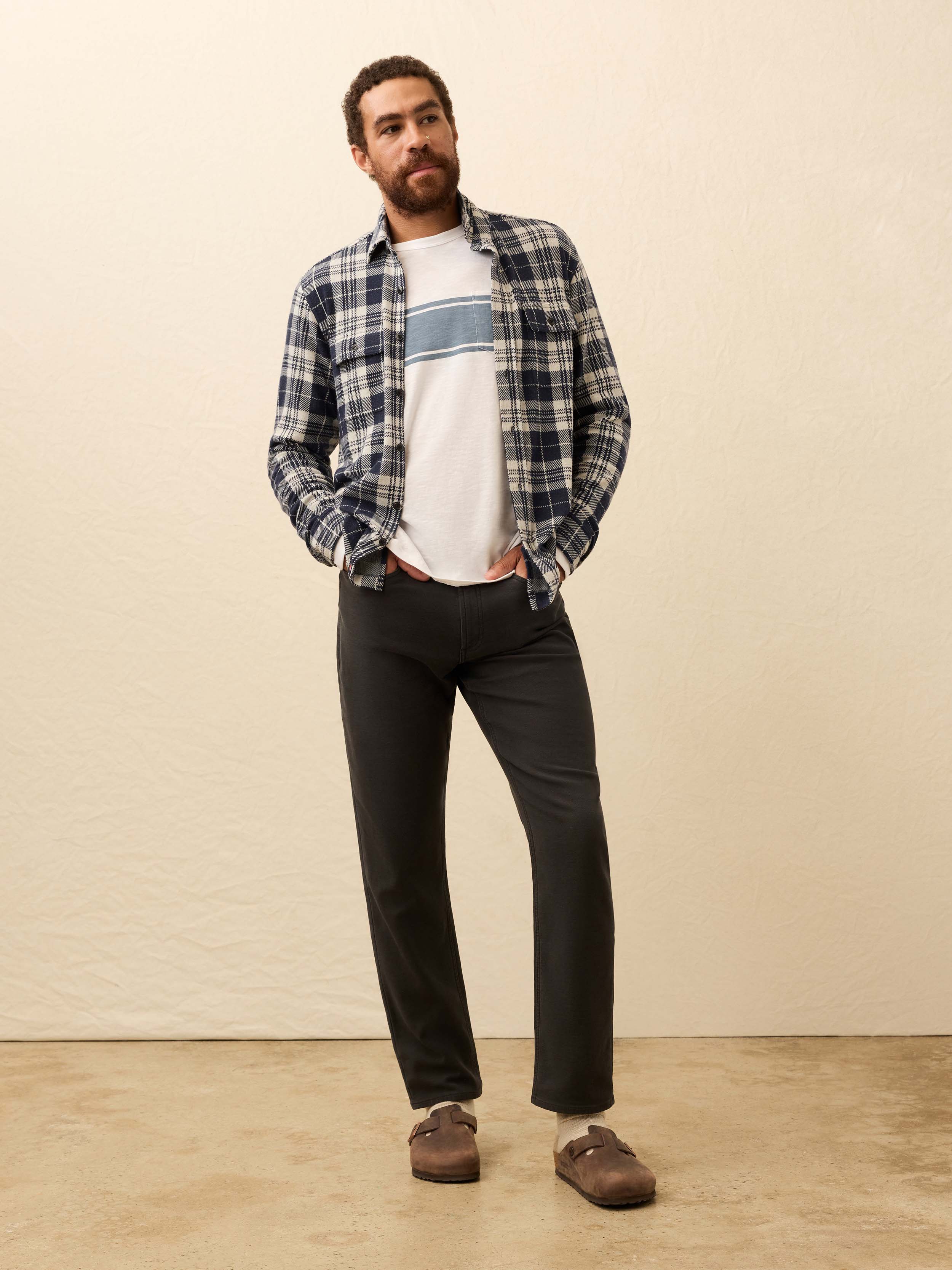 Man wearing a blue and white plaid shirt with dark jeans against a beige background