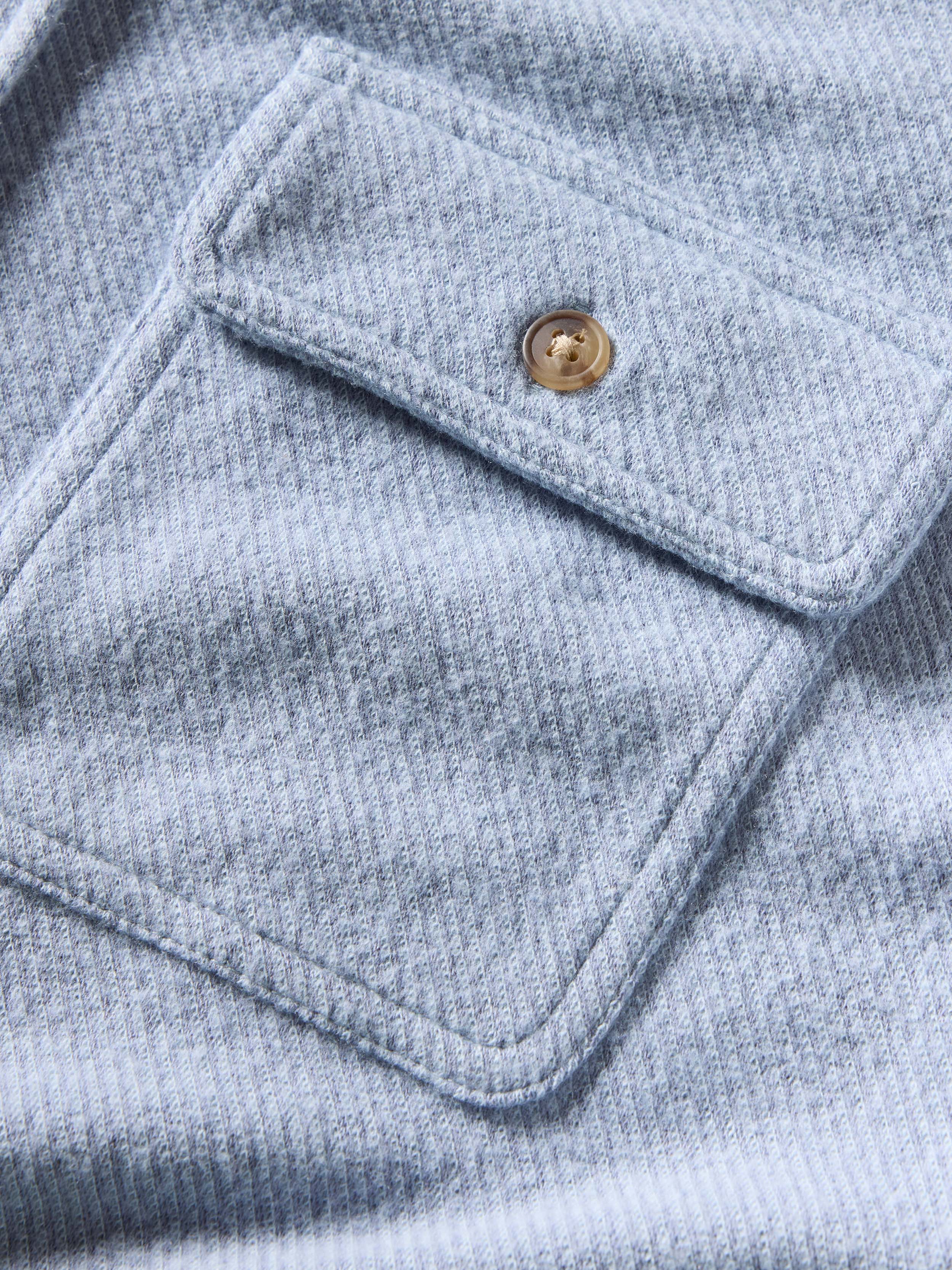 Close-up of a light blue textured shirt with a buttoned pocket