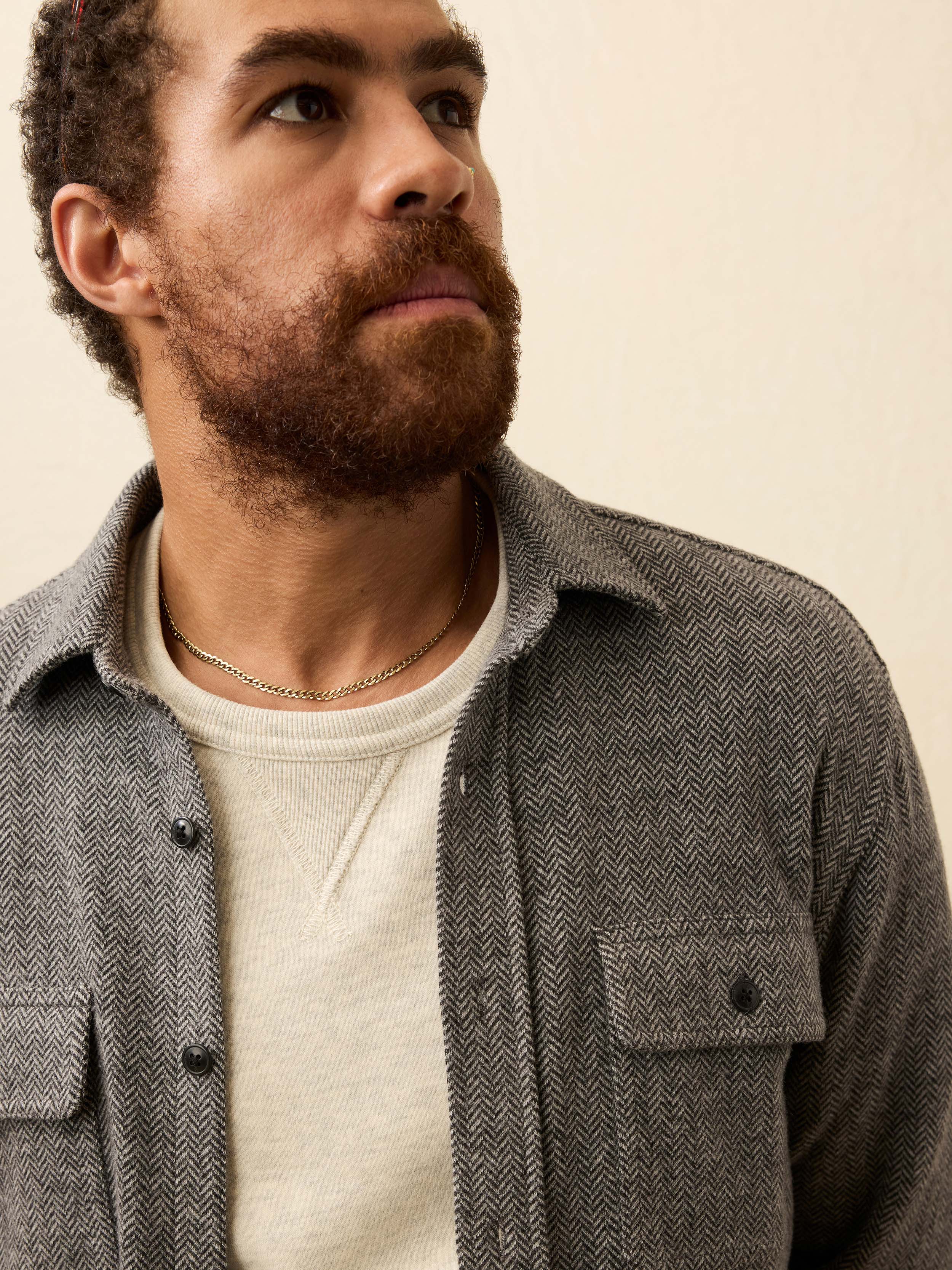 Man wearing a gray flannel shirt over a white sweater against a beige background