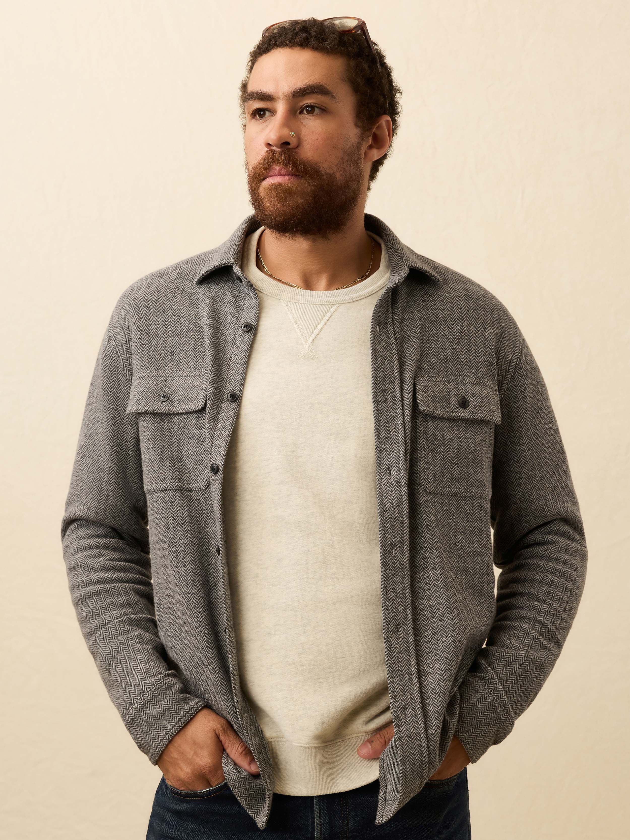 Man wearing a gray flannel shirt over a white sweater on a beige background