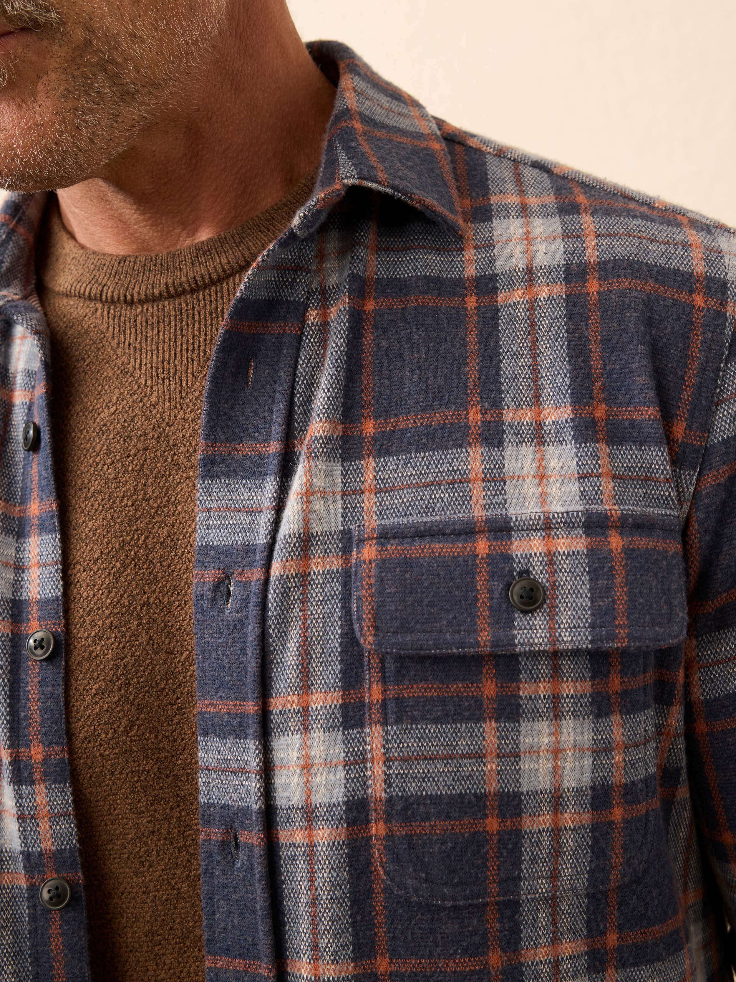 Close-up of a person wearing a blue plaid long sleeve shirt with a beige background