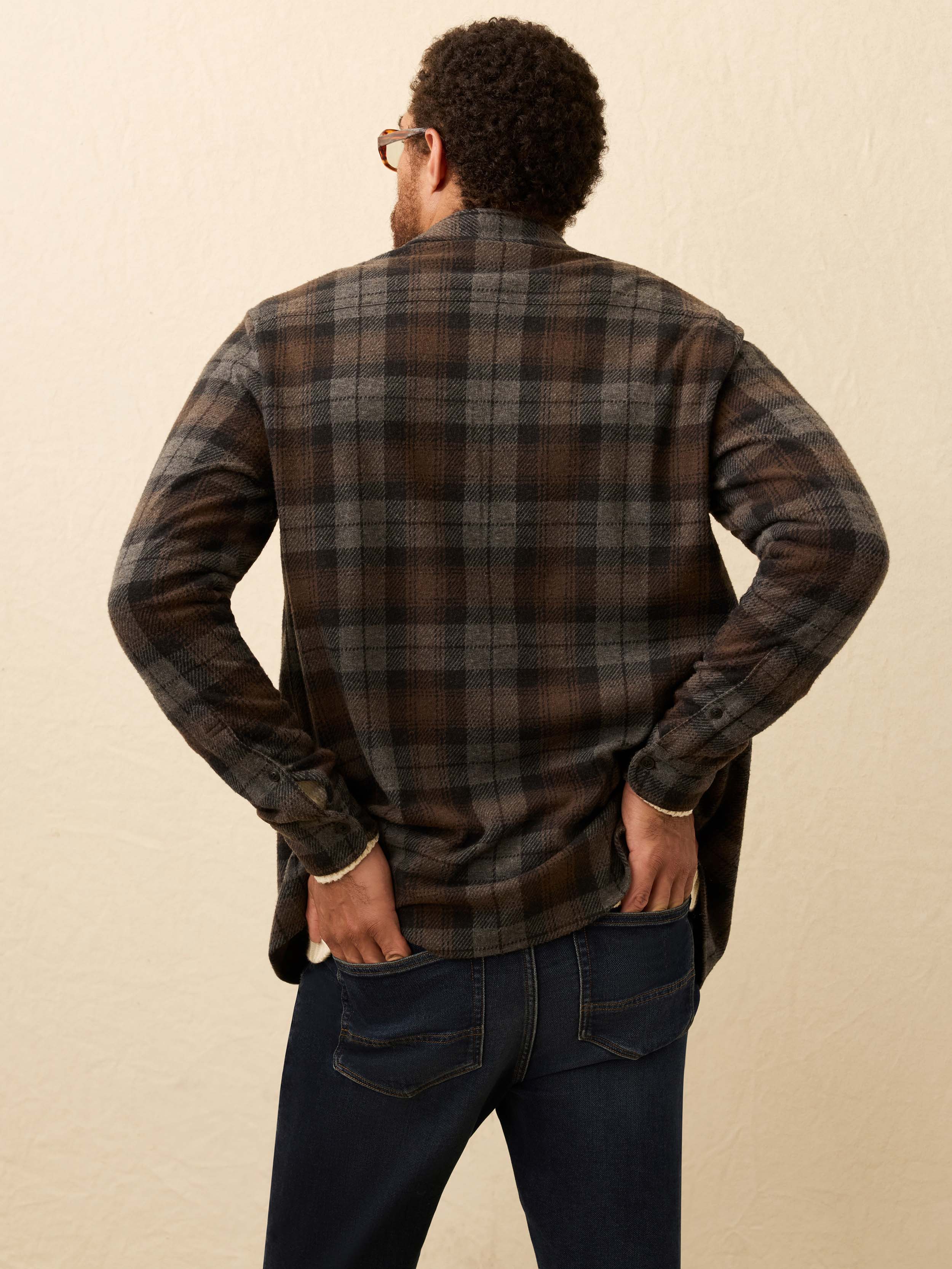 Man wearing a brown and grey plaid shirt, against a beige background