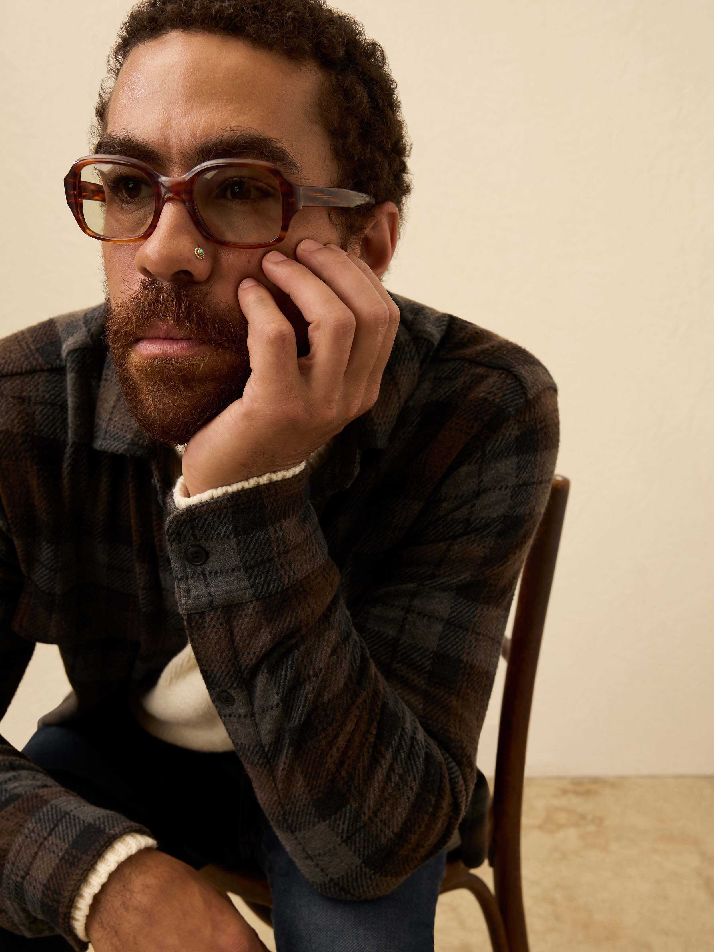 Man wearing a brown and grey plaid shirt, against a beige background