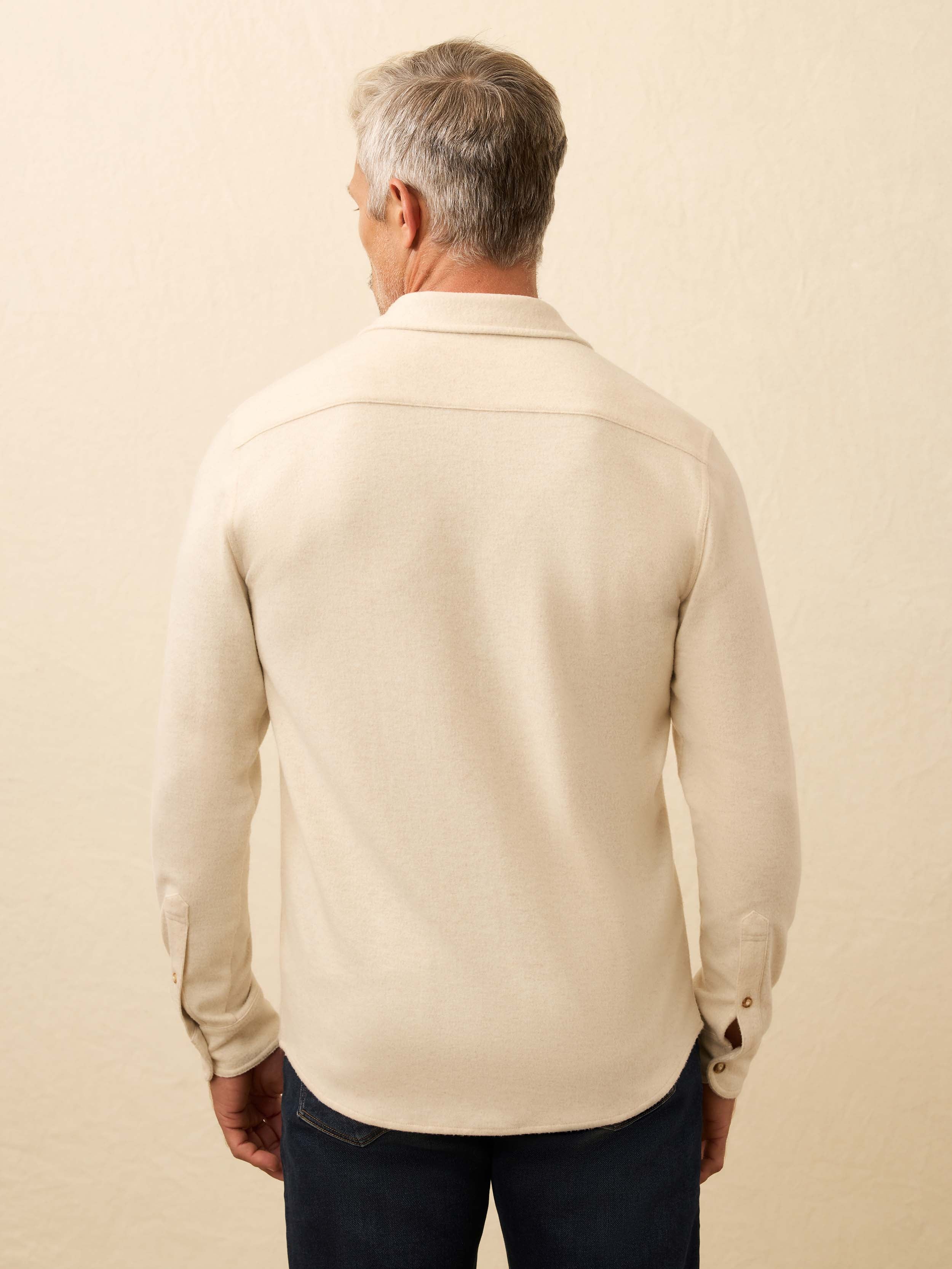 Man is wearing an ivory long sleeve button down shirt against a beige background