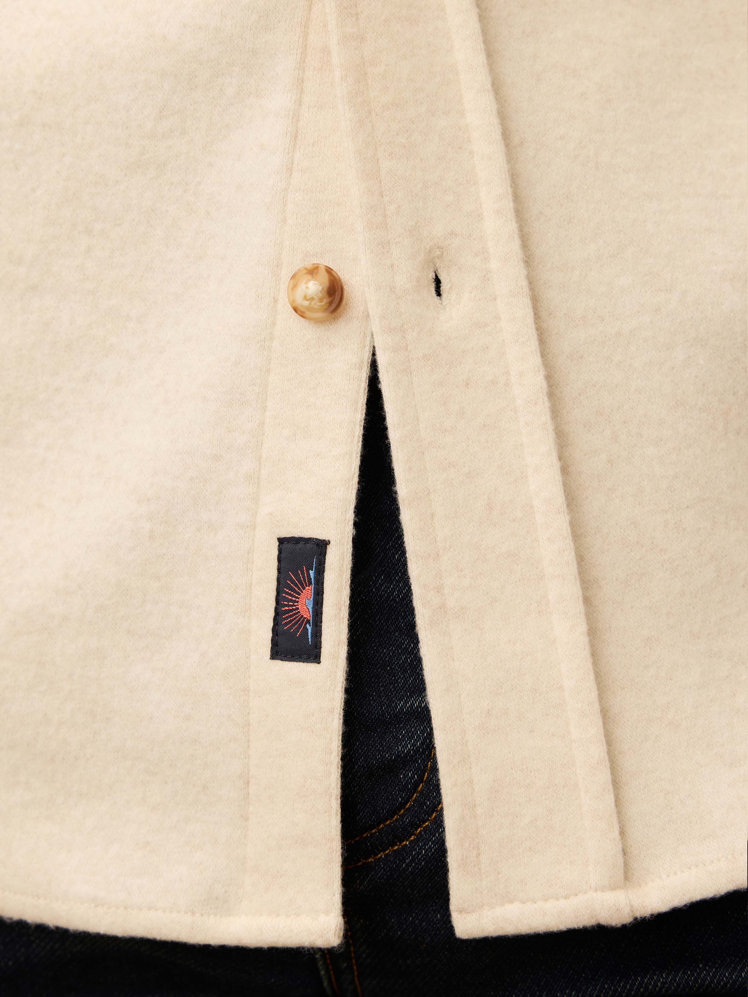 Close up of an ivory long sleeve button down shirt with Faherty brand logo at the placket 