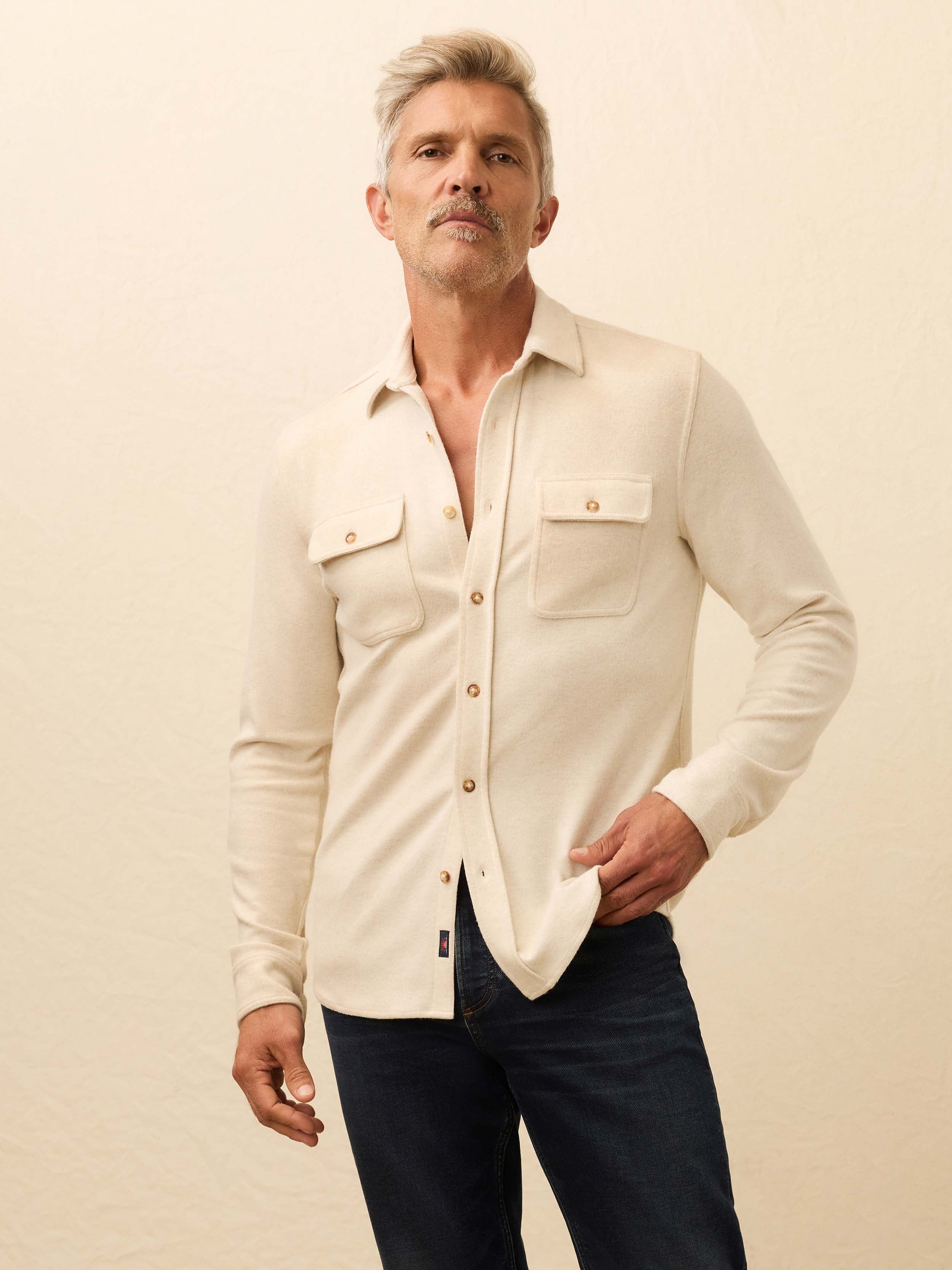 Man is wearing an ivory long sleeve button down shirt against a beige background