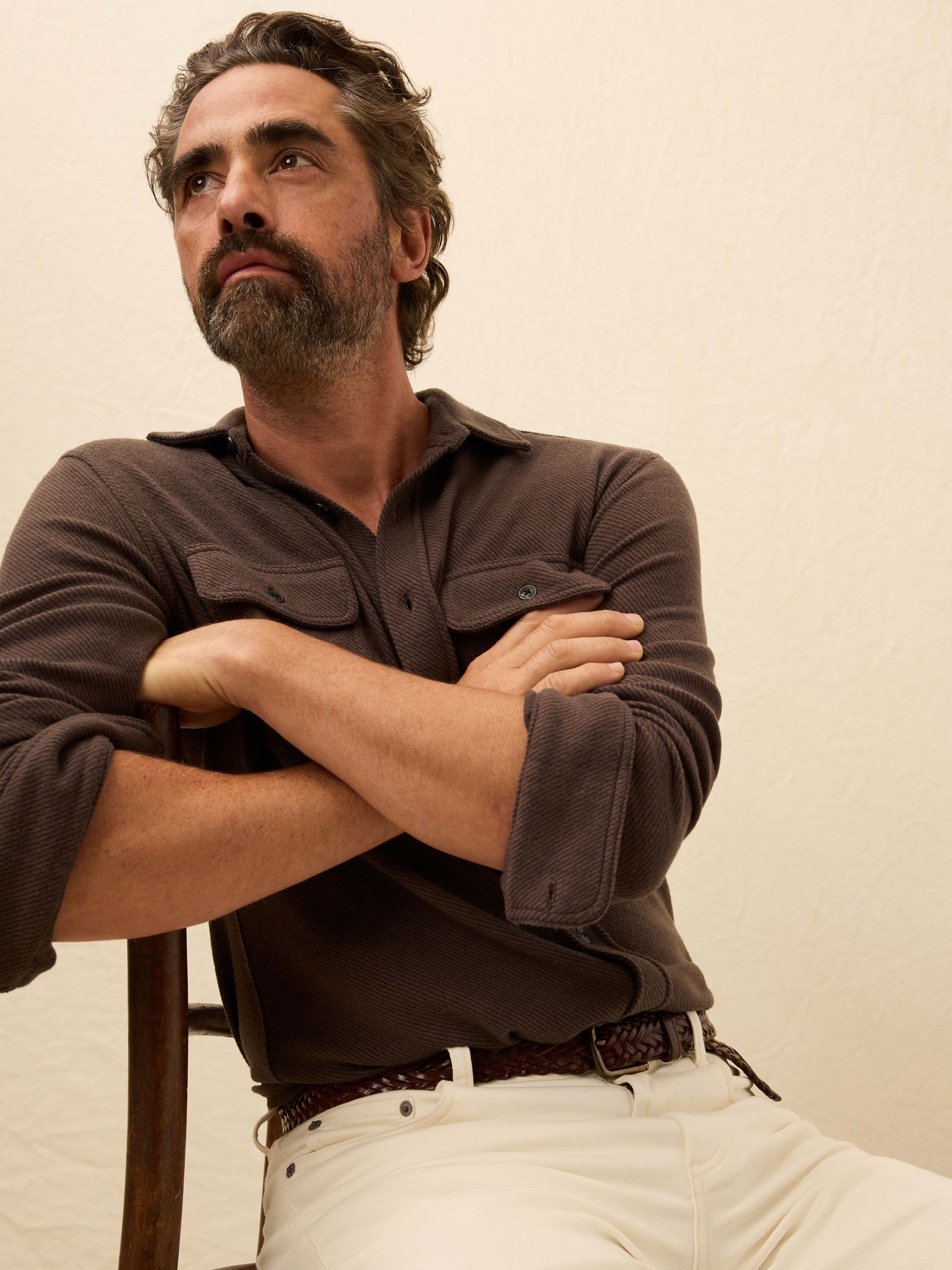Man wearing a brown button up shirt against a beige background