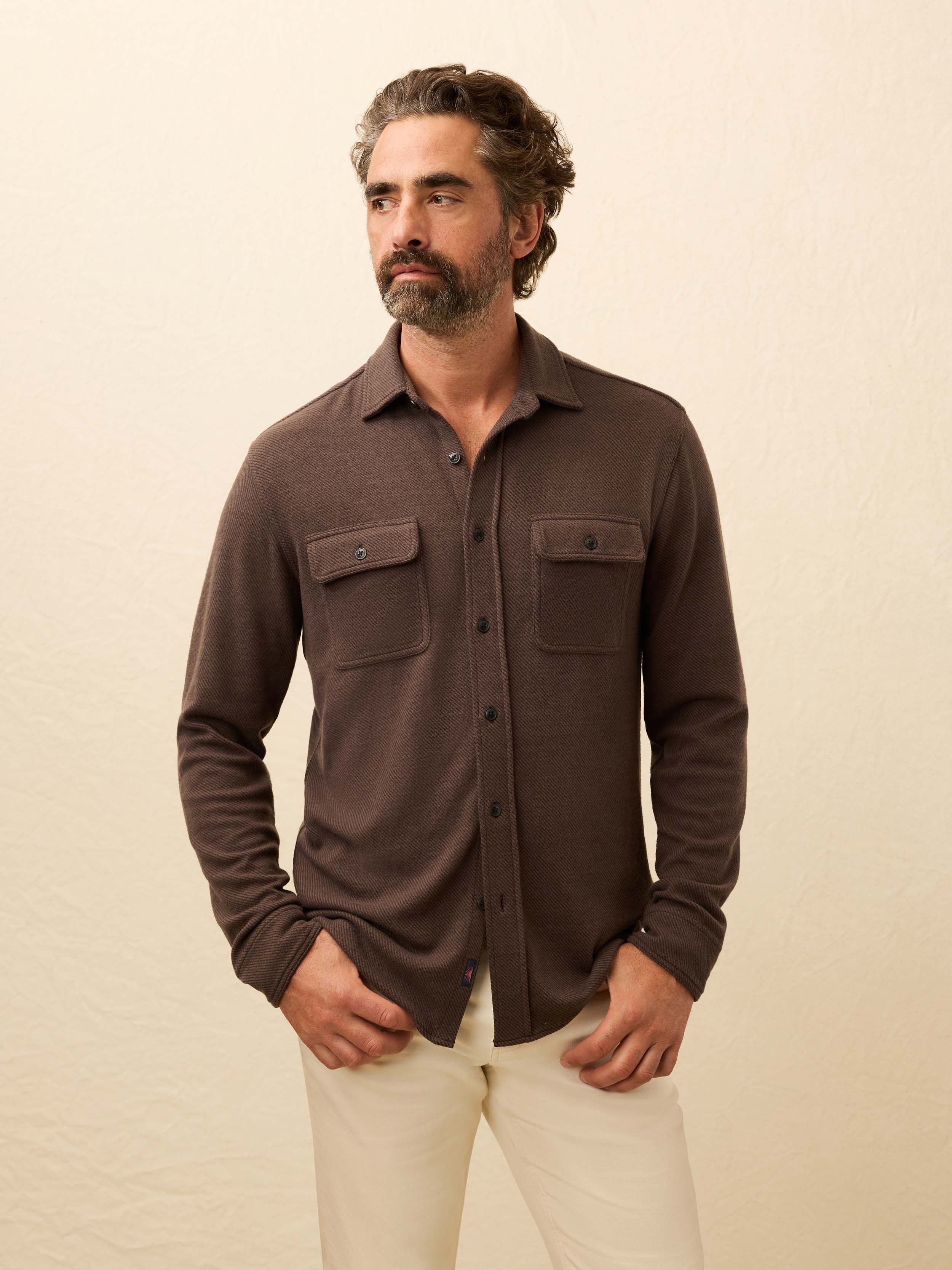 Man wearing a brown button up shirt against a beige background