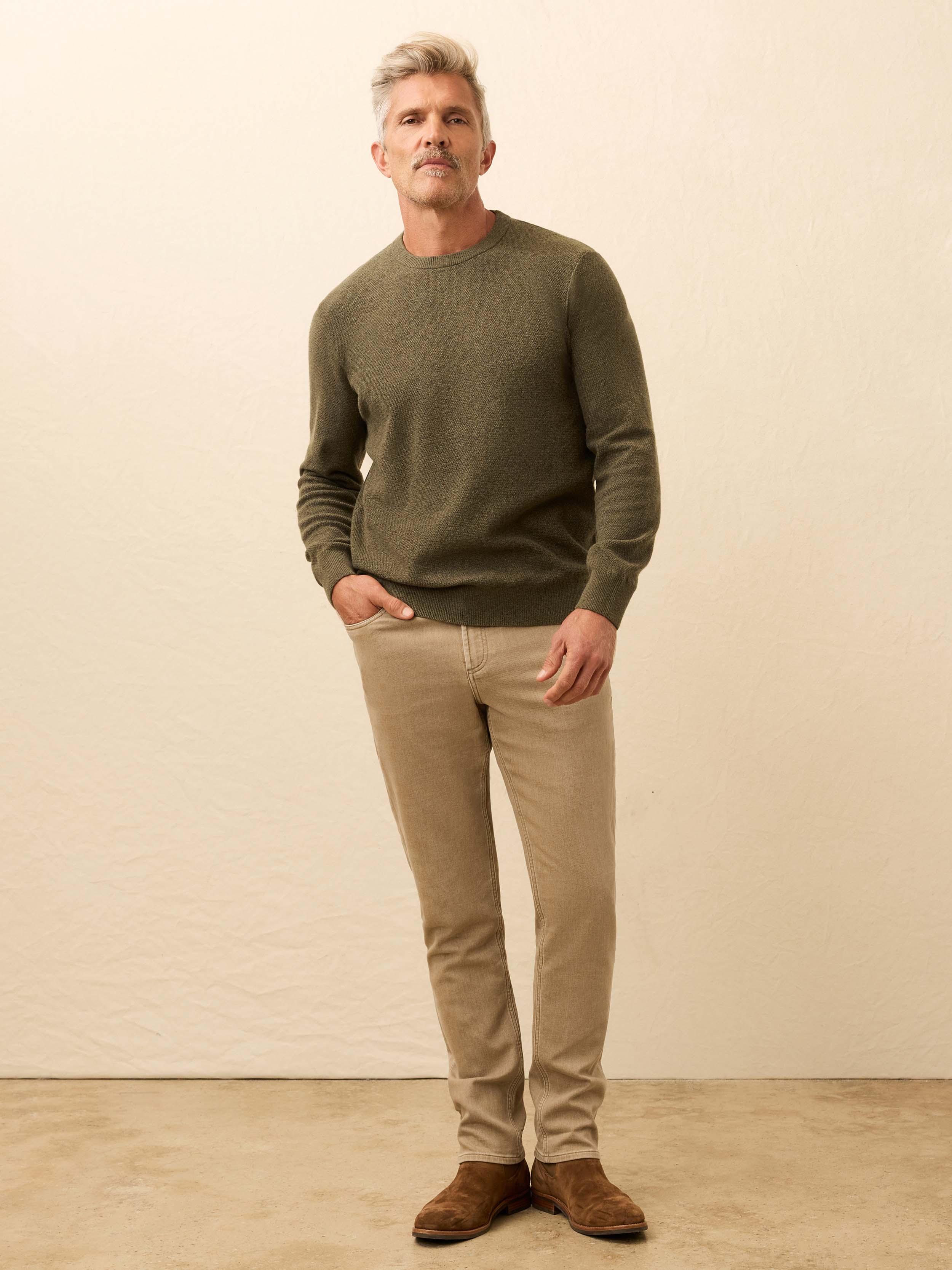 Man is wearing a green crewneck sweater with beige pants against a beige background