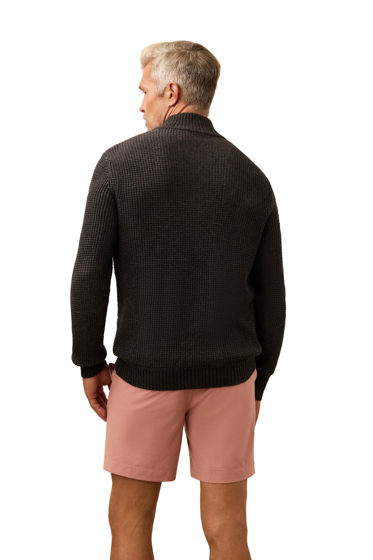 A man viewed from behind wearing a dark grey sweater and salmon colored shorts, image 3 of 3