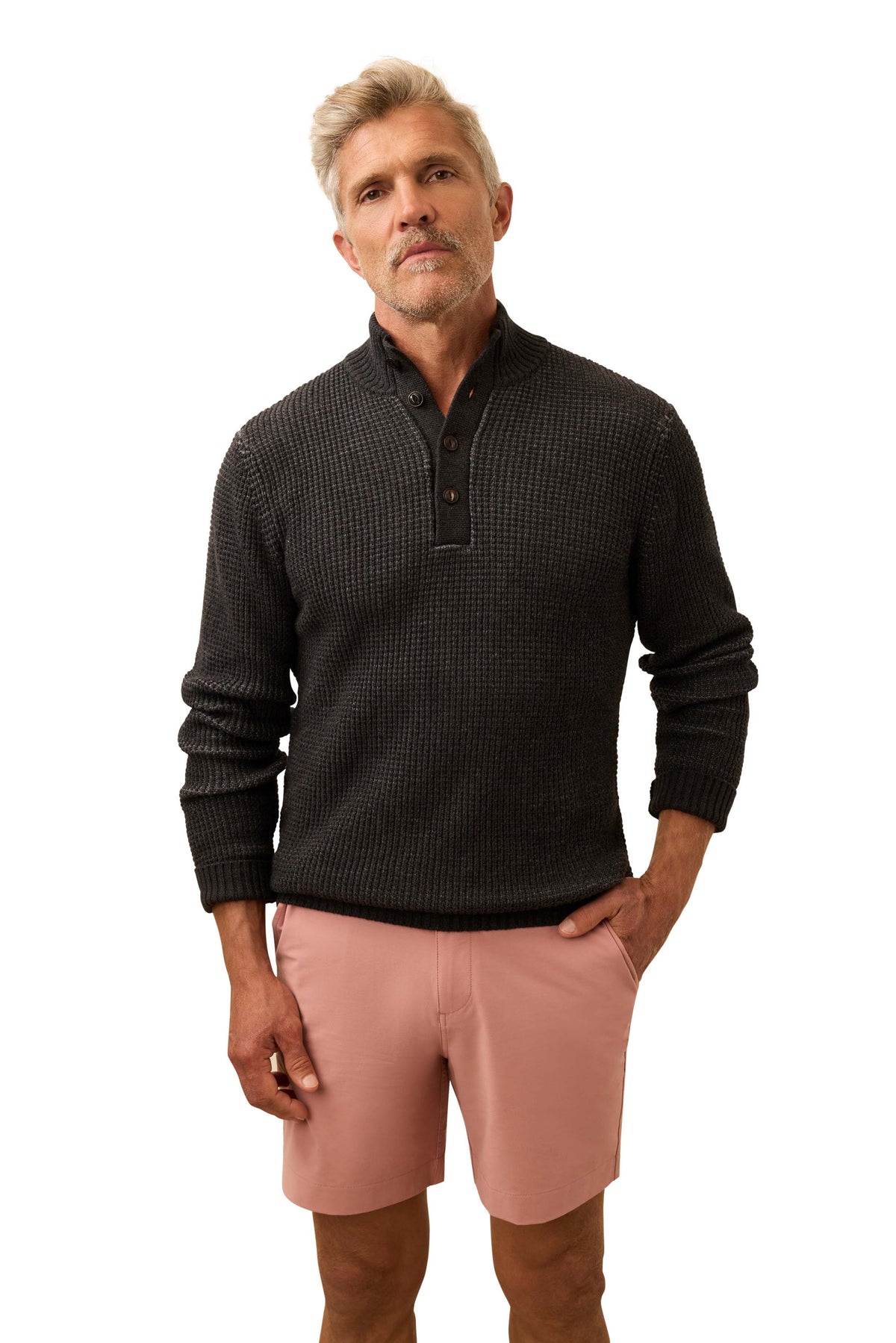 A man wearing a dark grey sweater and salmon colored shorts, image 1 of 3