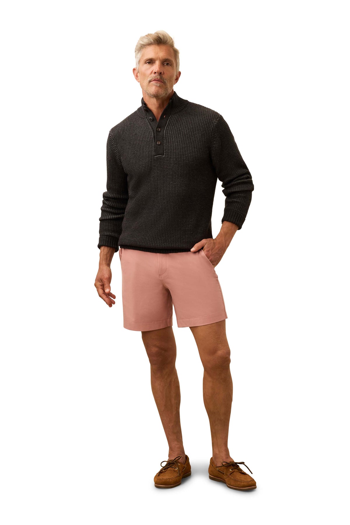 A man wearing a dark grey sweater and salmon colored shorts, image 2 of 3