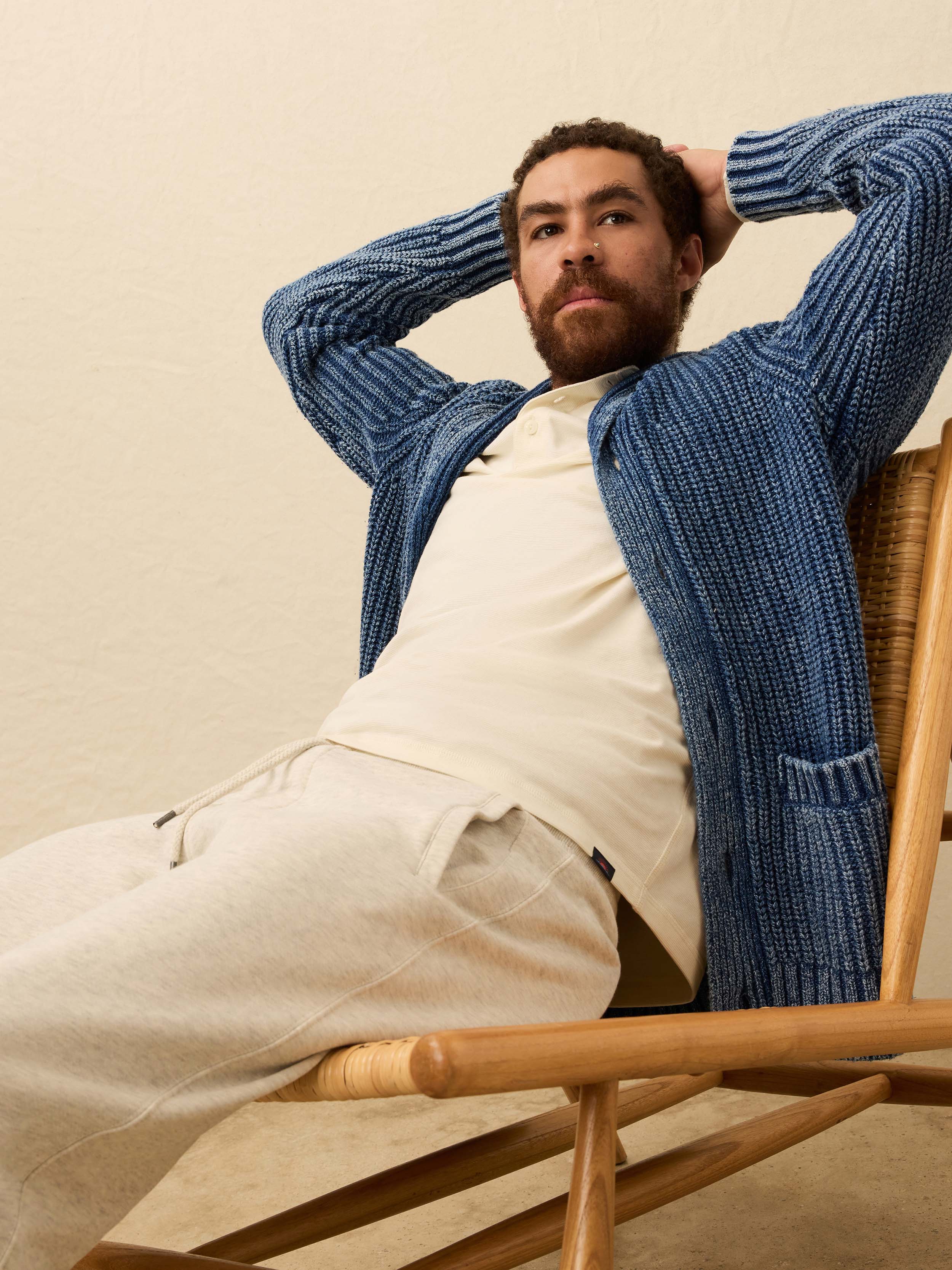 Man wearing a blue cardigan over a white henley shirt against a beige background