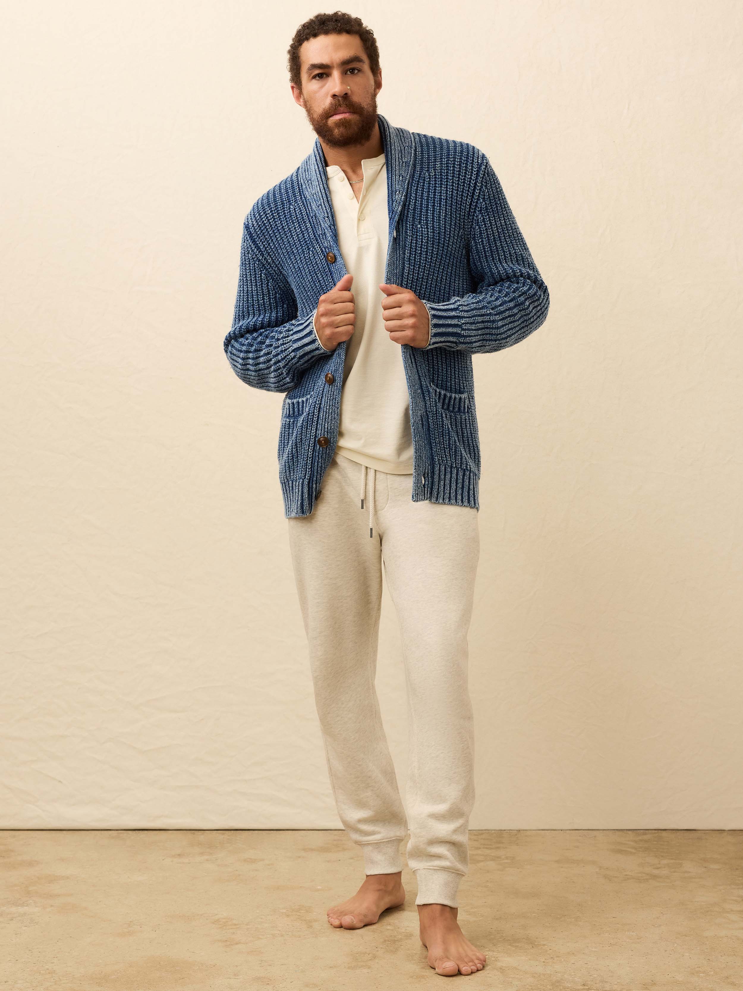 Man wearing a blue cardigan over a white henley shirt against a beige background