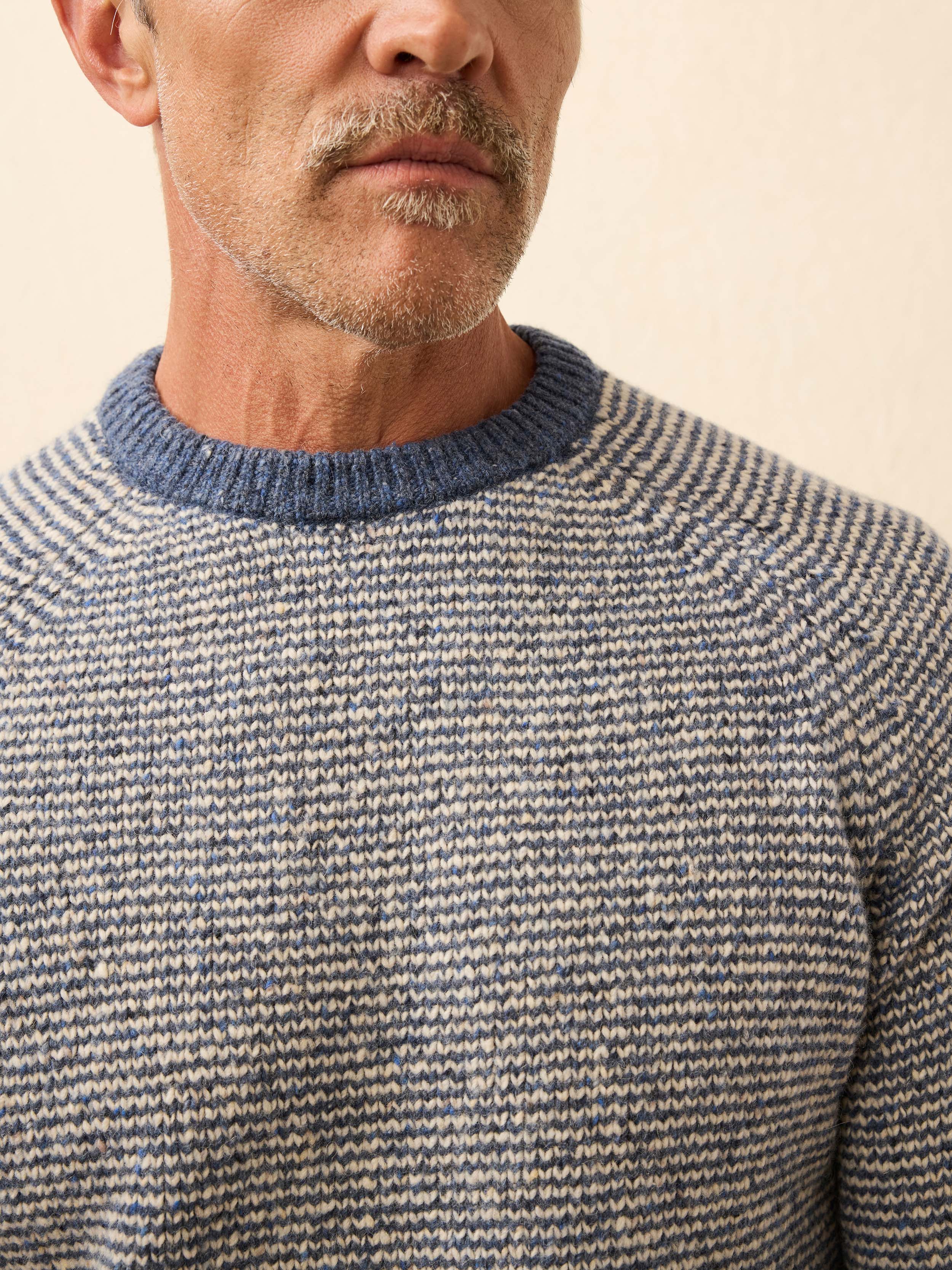 Man is wearing a blue and white sweater against a beige background