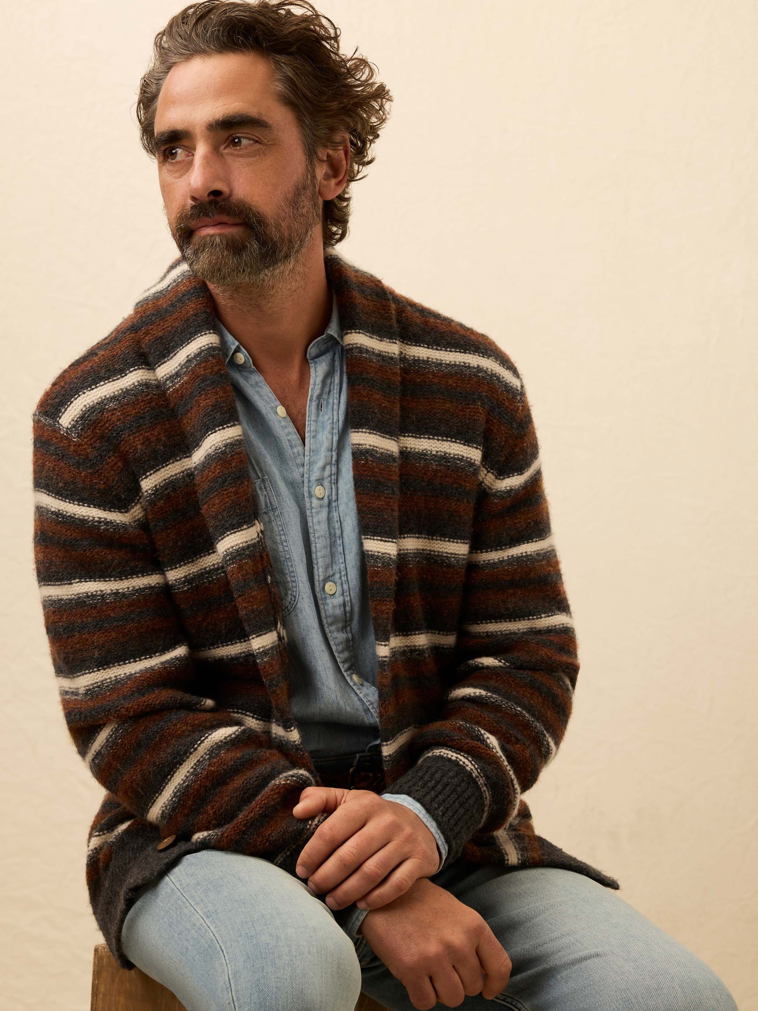Man wearing a brown striped cardigan over a chambray shirt against a beige background
