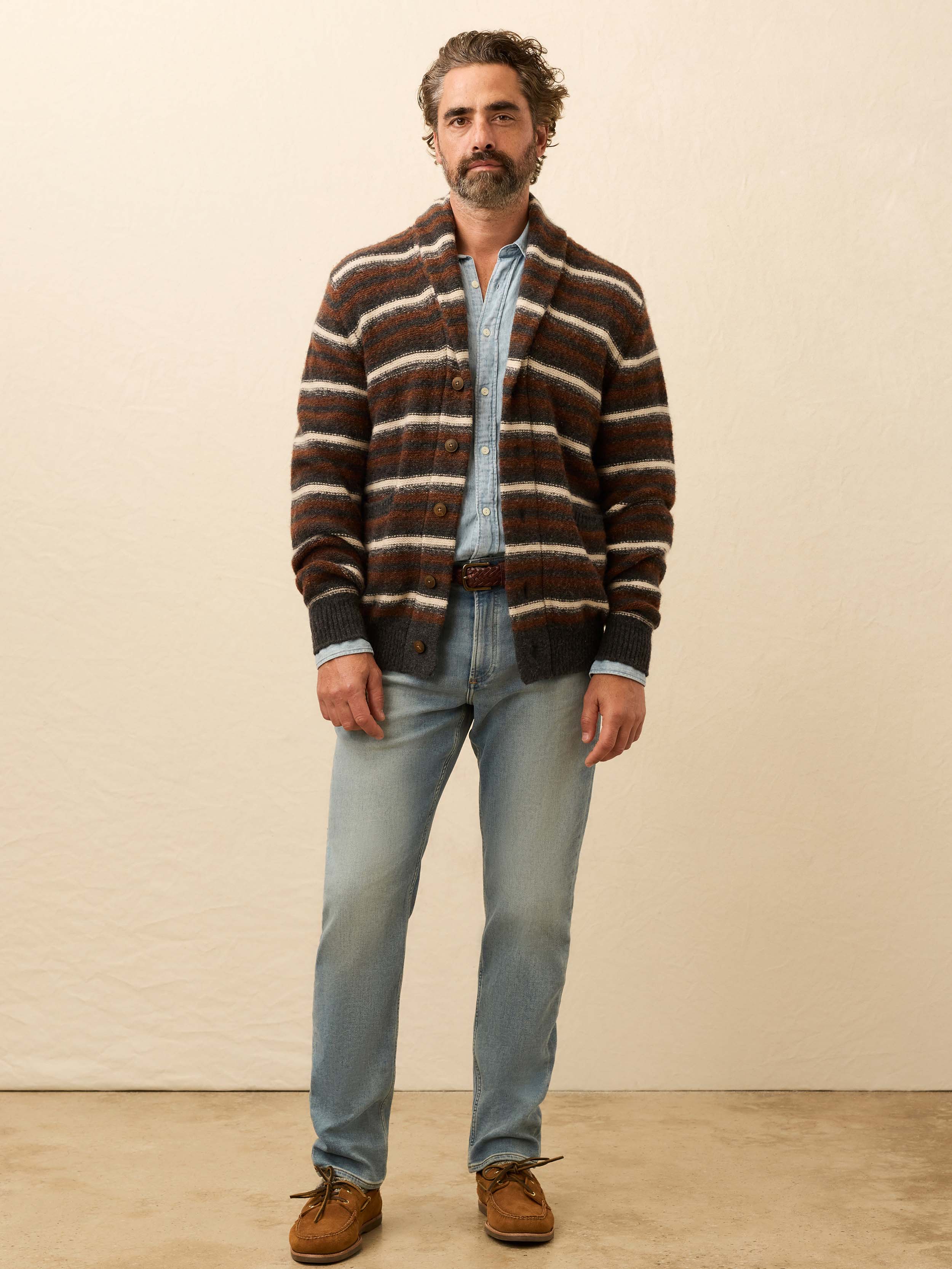 Man wearing a brown striped cardigan over a chambray shirt against a beige background
