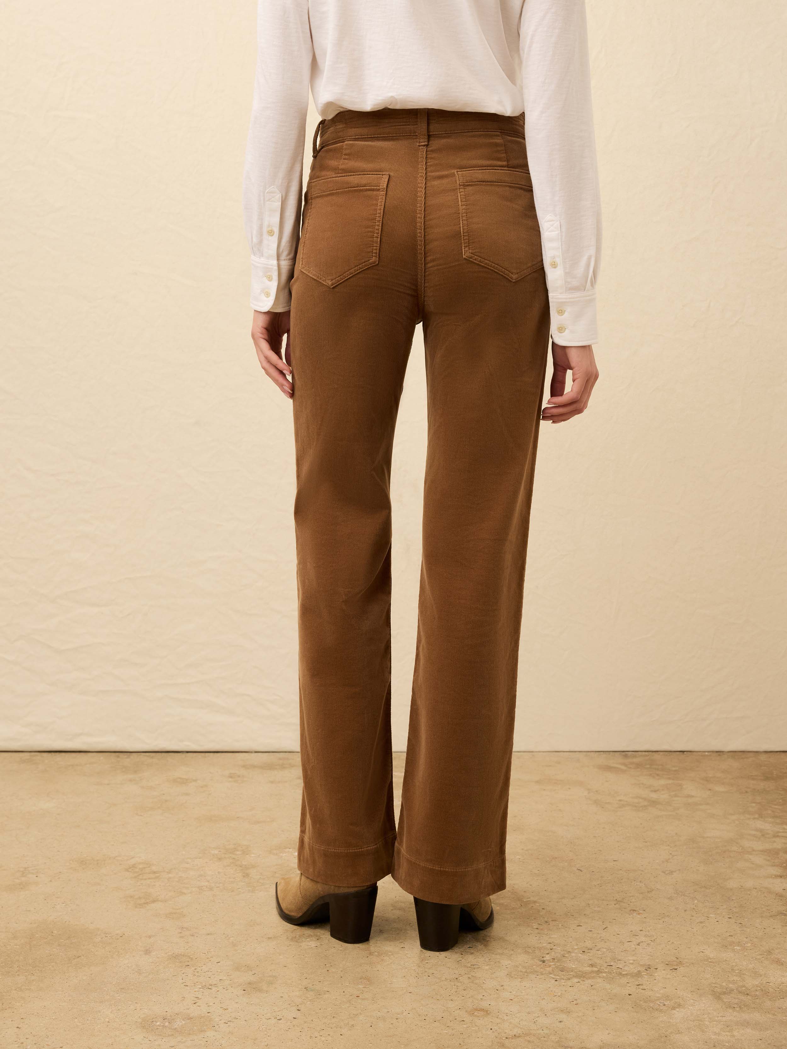 Woman is wearing brown corduroy pants with a white shirt against a beige background