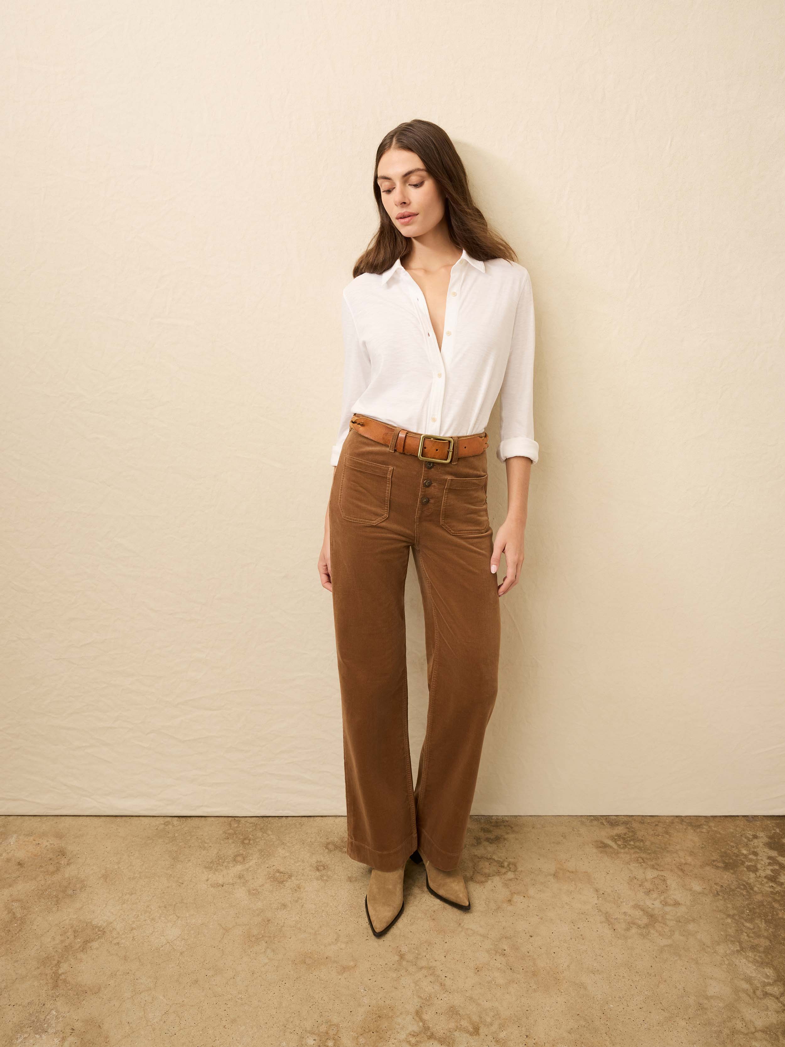 Woman is wearing brown corduroy pants with a white shirt against a beige background
