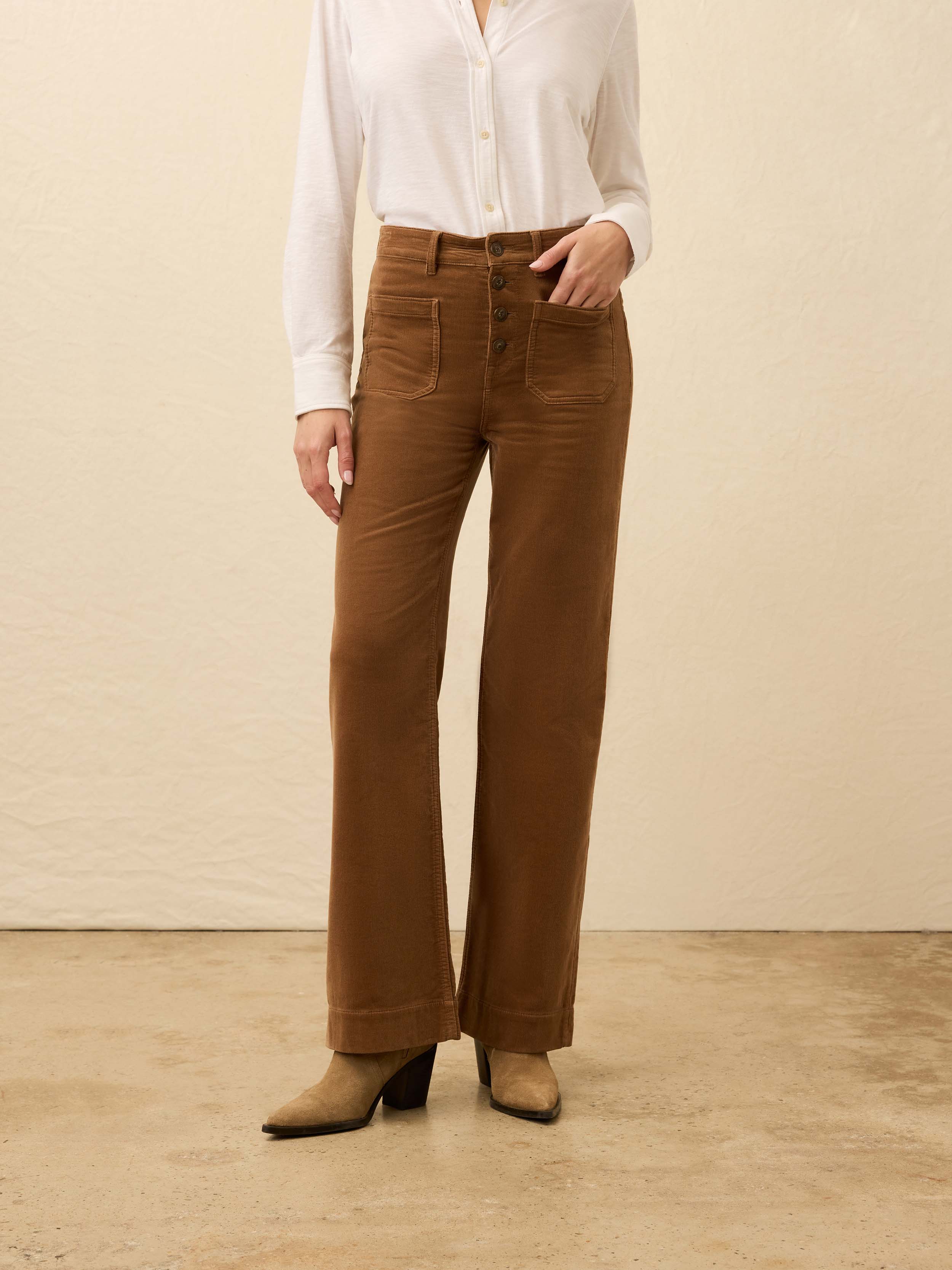Woman is wearing brown corduroy pants with a white shirt against a beige background