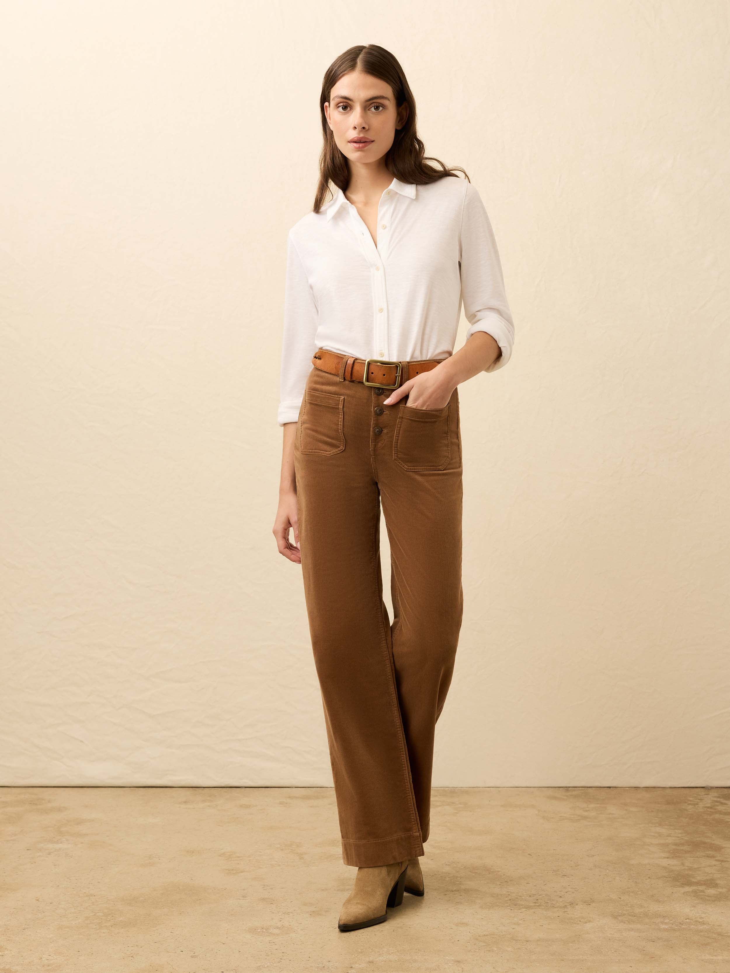 Woman is wearing brown corduroy pants with a white shirt against a beige background