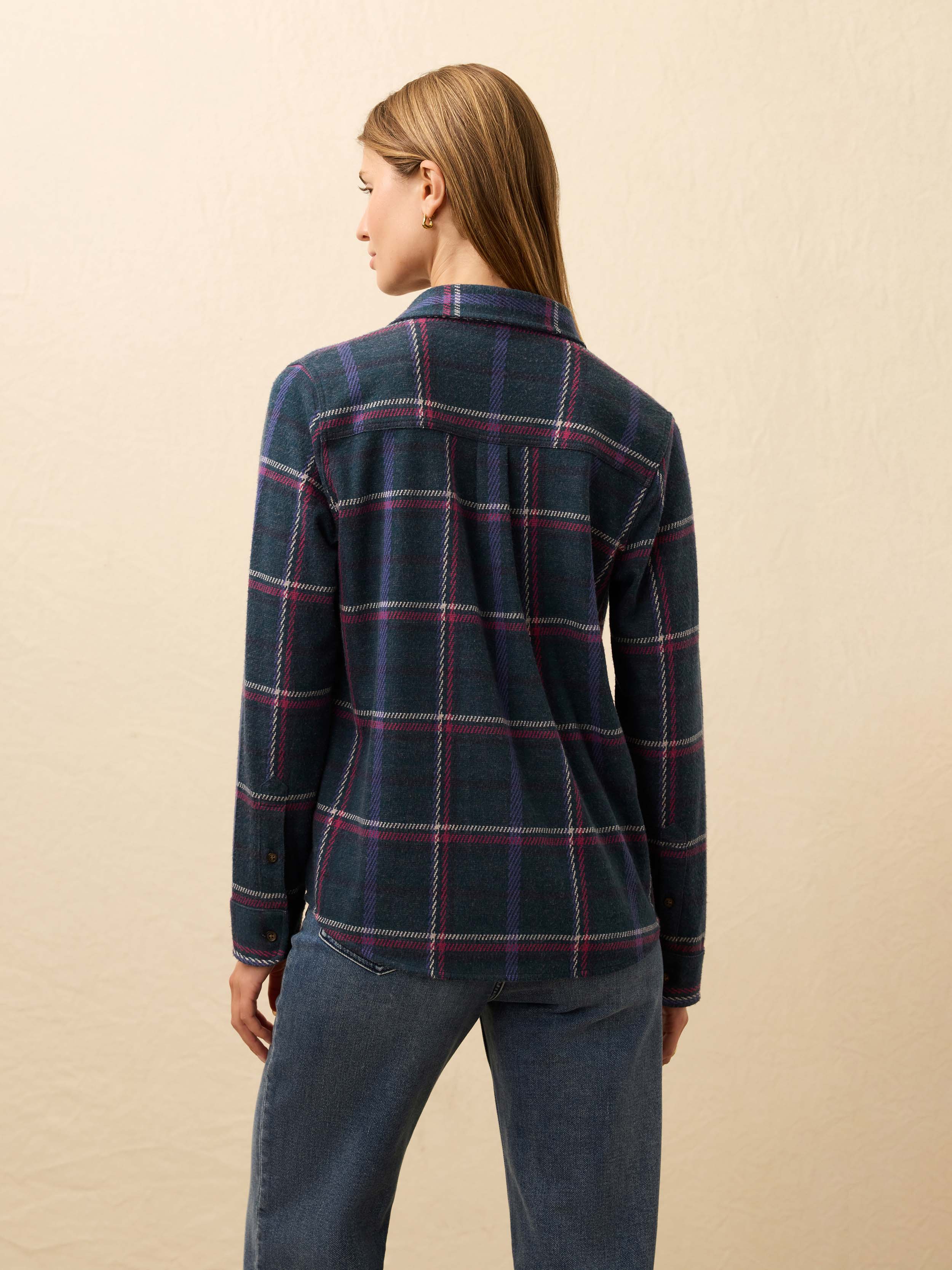 Woman is wearing a navy and burgundy plaid flannel against a beige background