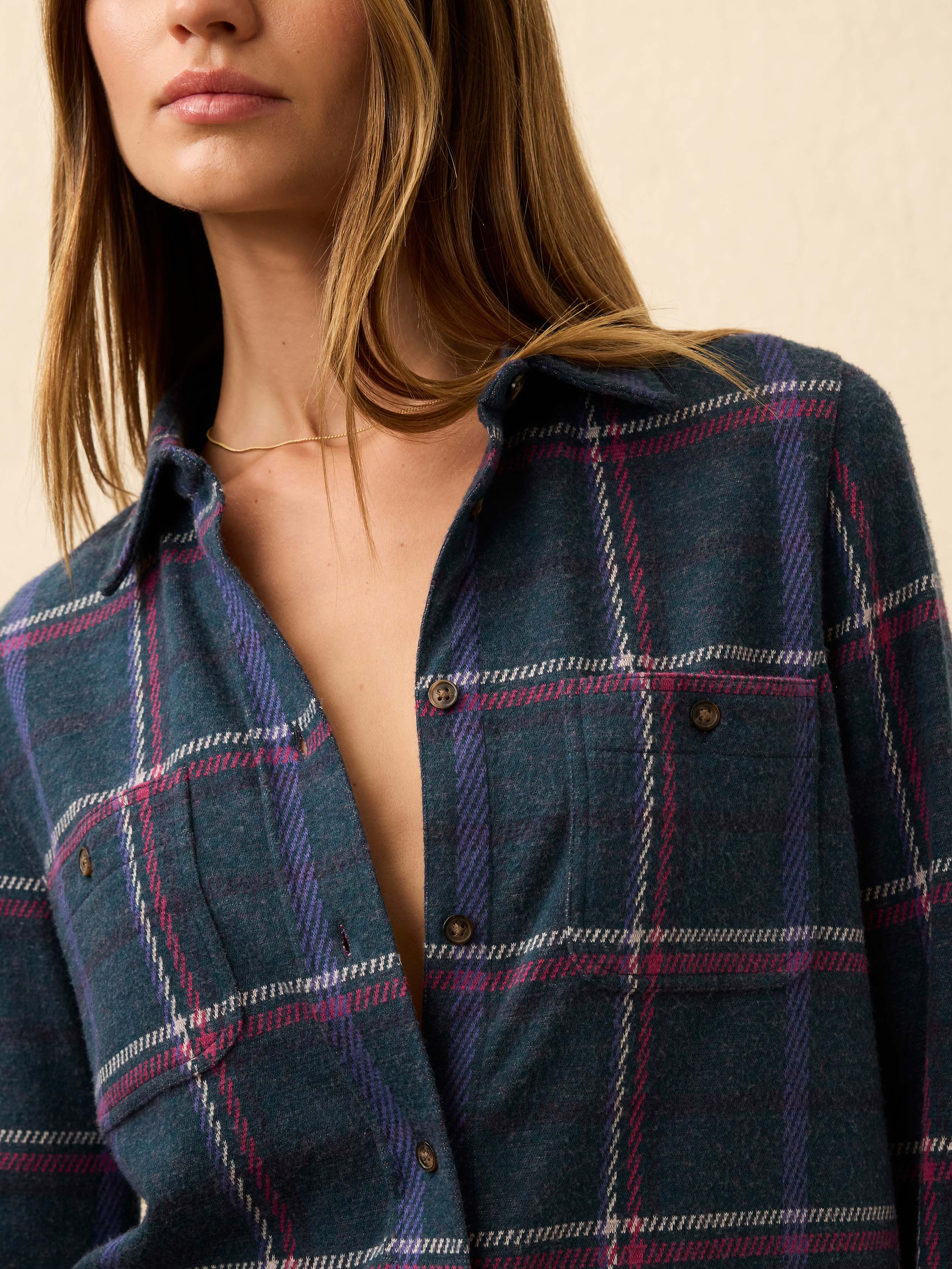 Woman is wearing a navy and burgundy plaid flannel against a beige background