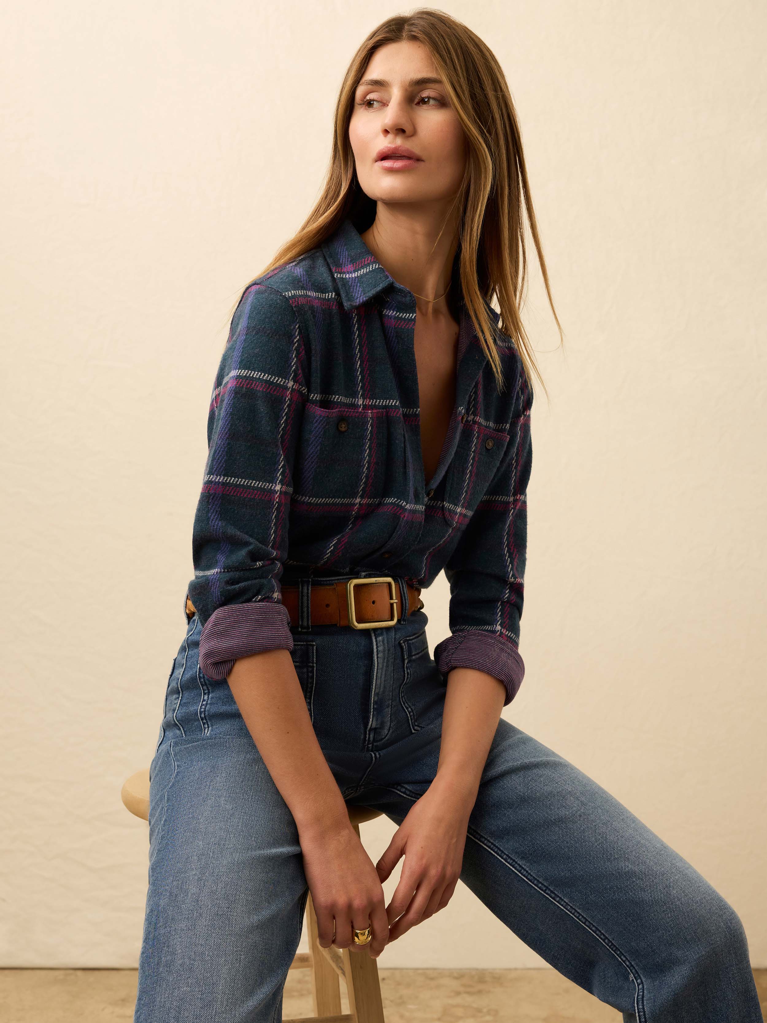 Woman is wearing a navy and burgundy plaid flannel against a beige background