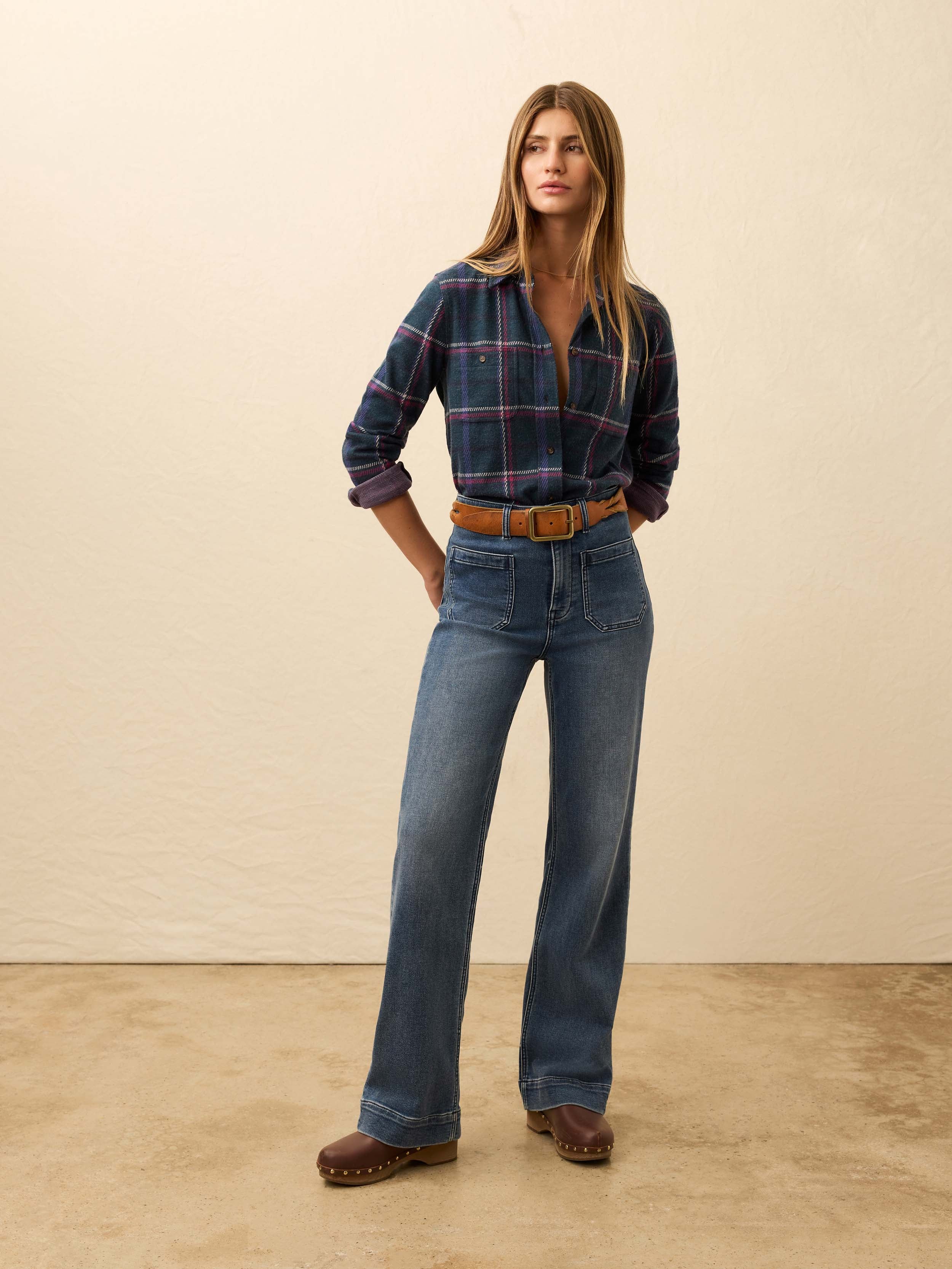 Woman is wearing a navy and burgundy plaid flannel against a beige background