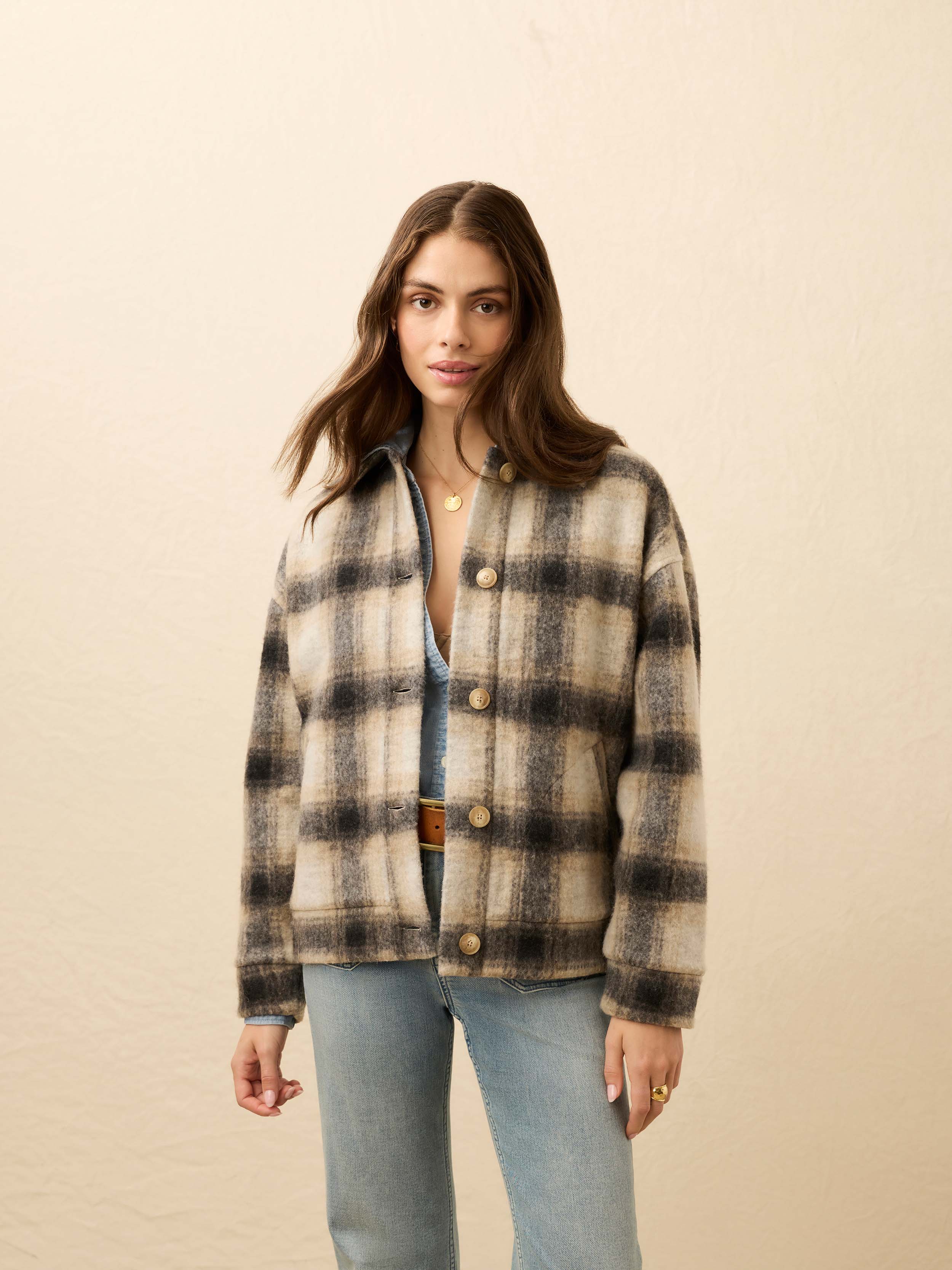 Woman wearing a plaid jacket over a denim top on a beige background