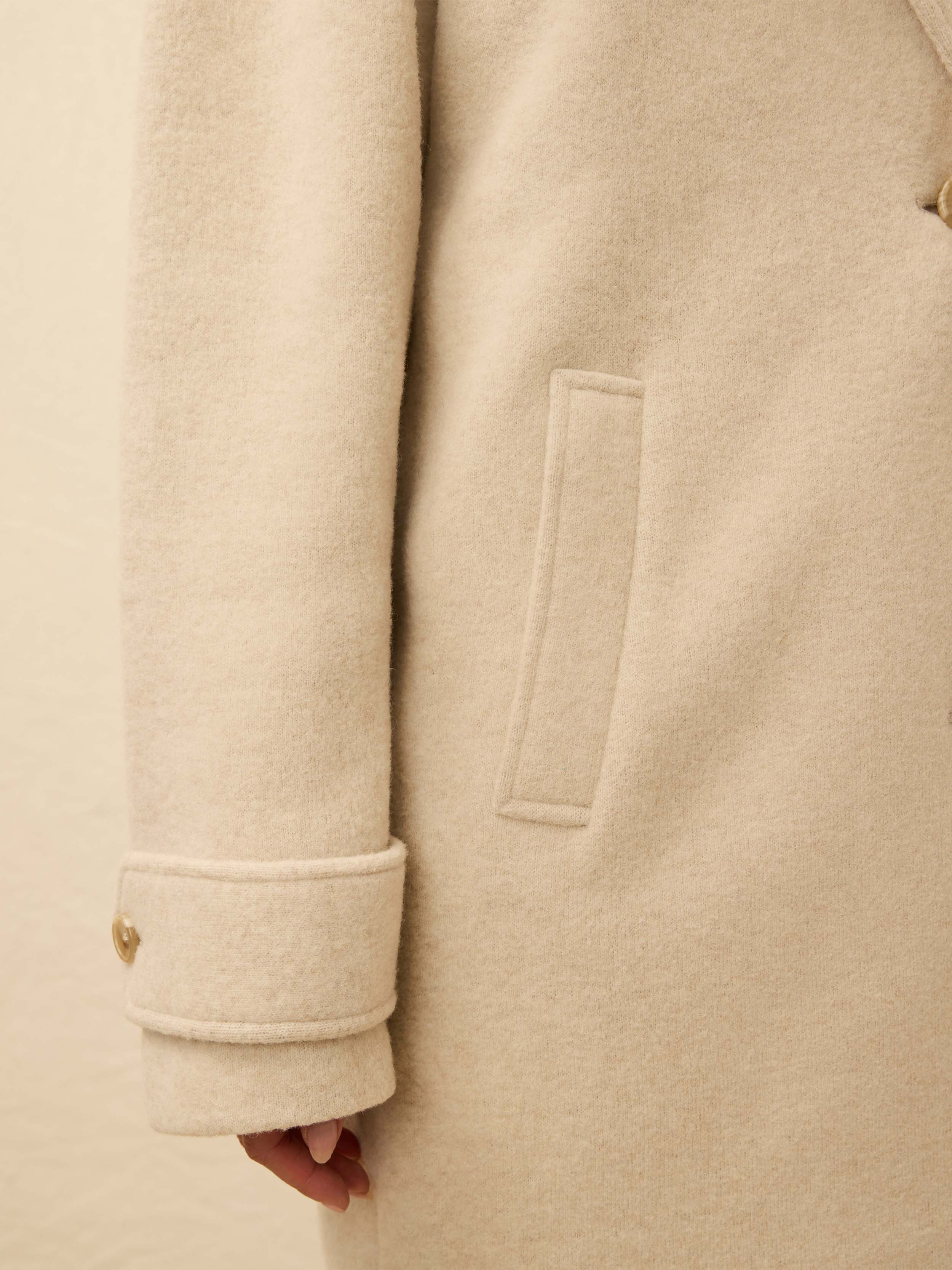 Close-up of a beige coat with a pocket detail on a neutral background