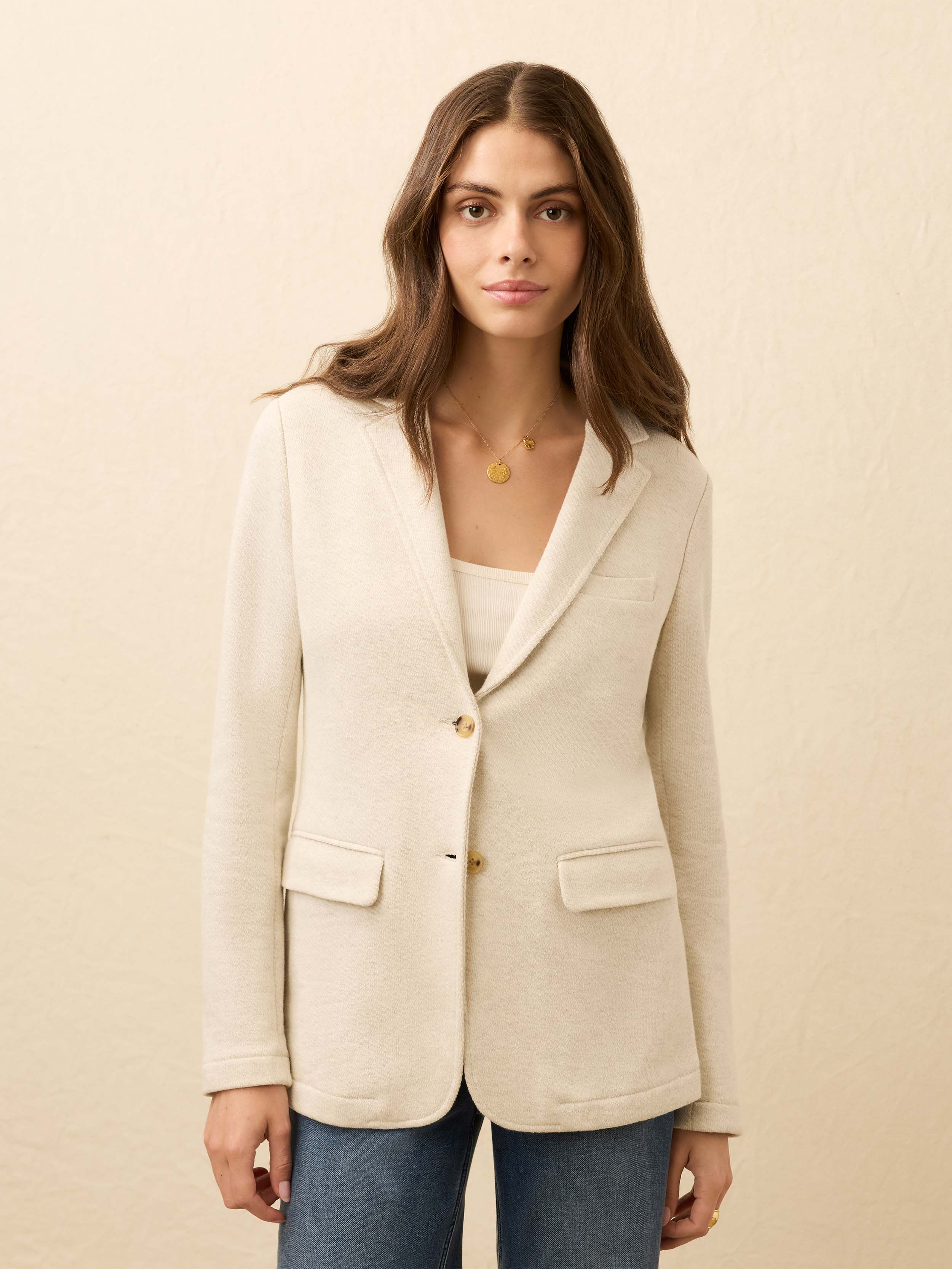 Woman wearing a heather grey blazer and blue jeans against a beige background