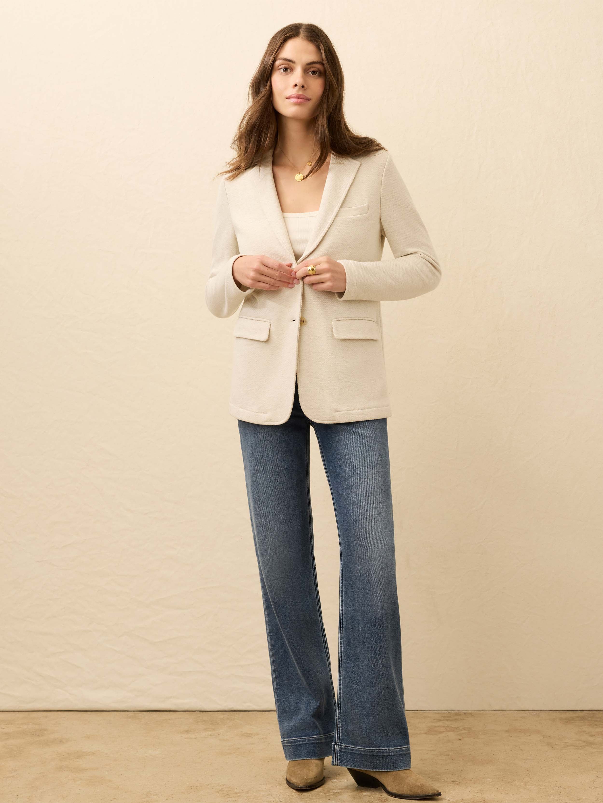 Woman wearing a heather grey blazer and blue jeans against a beige background