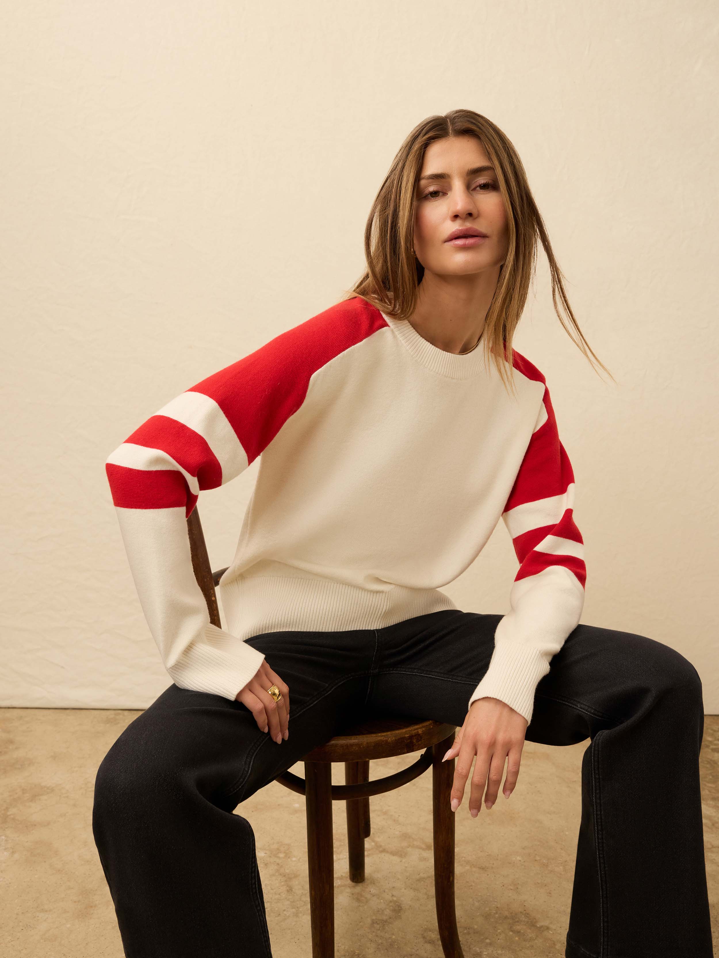 Woman wearing a red and white striped sweater sitting on a chair against a beige wall.