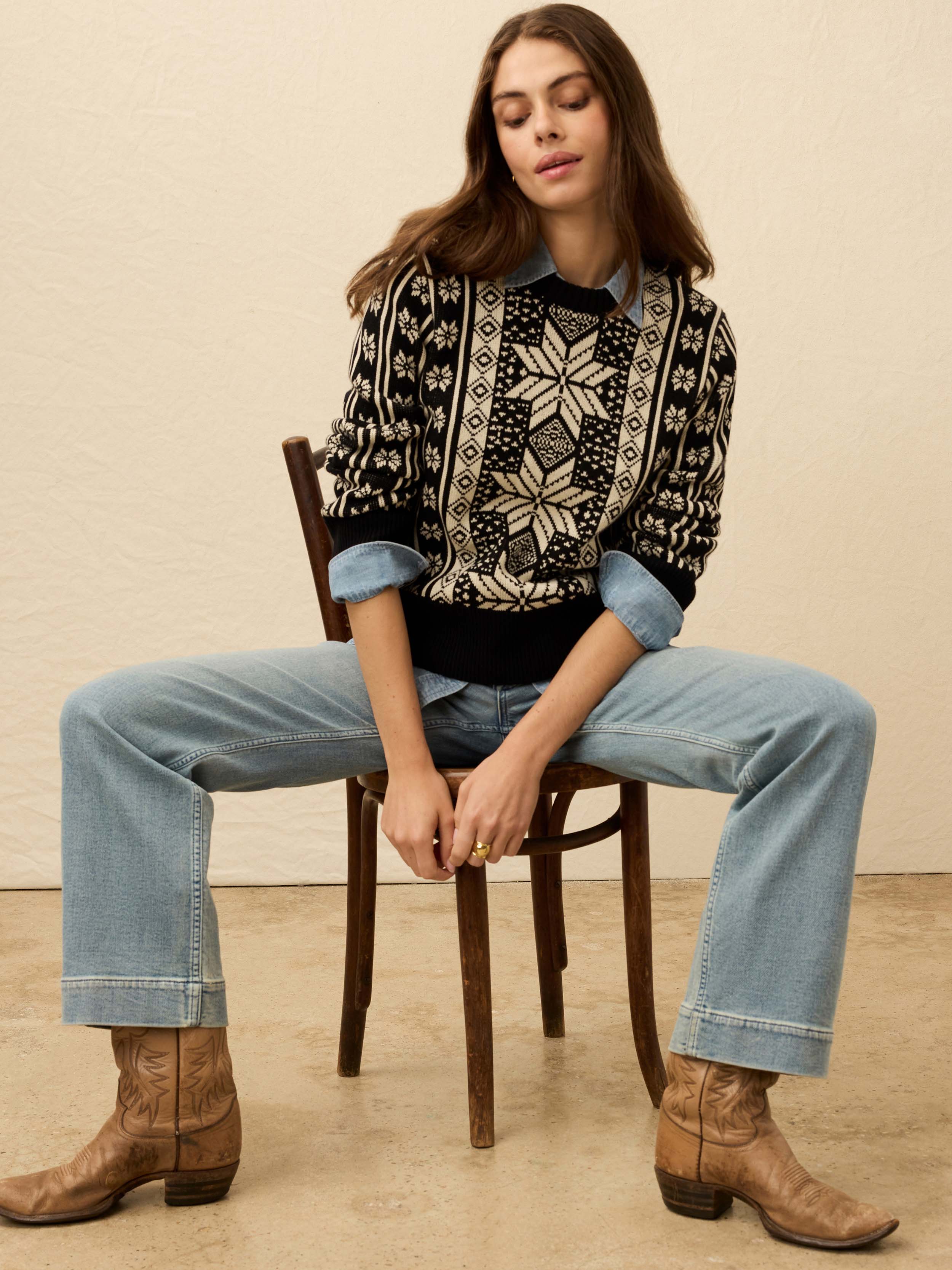 Woman wearing a black and white patterned sweater and jeans against a beige background