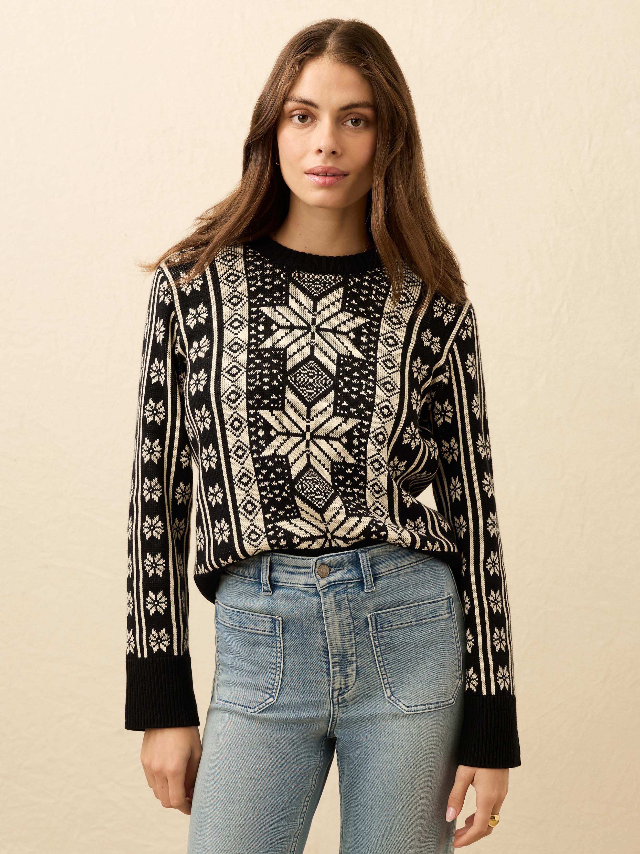 Woman wearing a black and white patterned sweater with jeans on a beige background