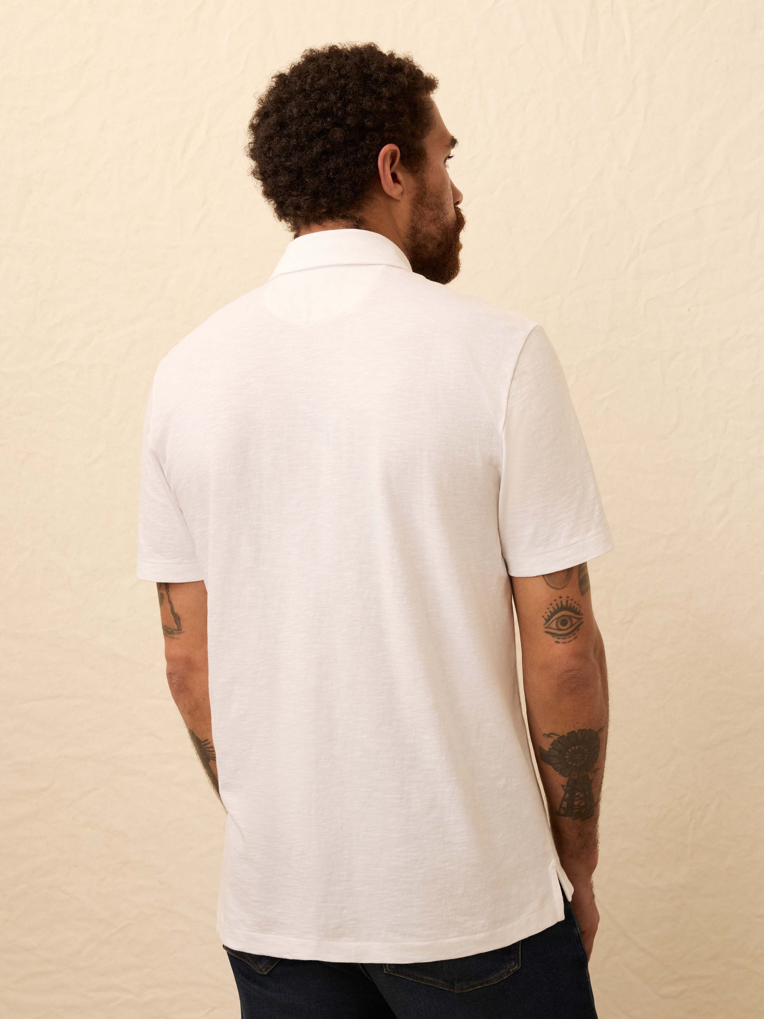 Man wearing a white polo shirt and dark jeans against a beige background