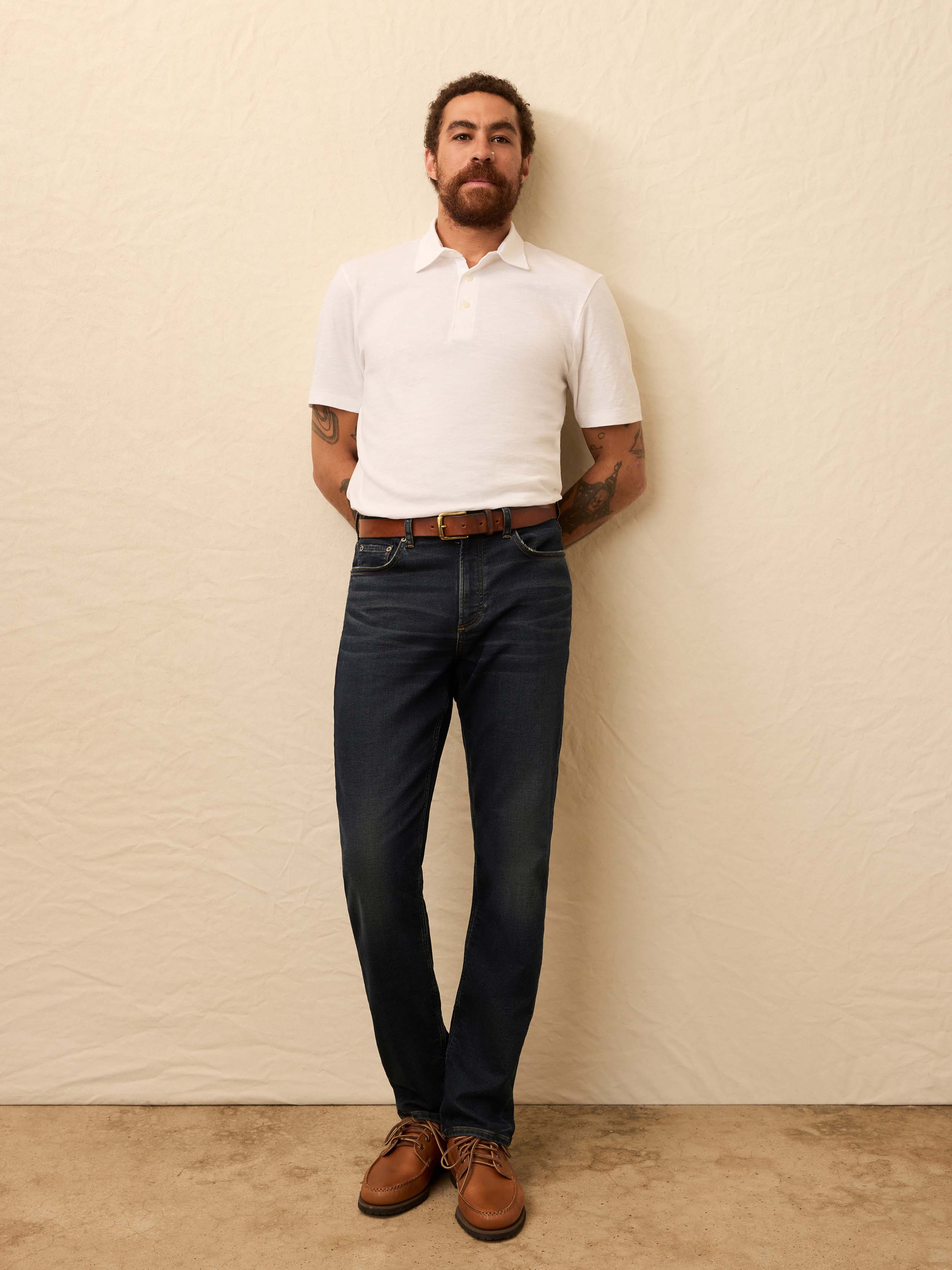 Man wearing a white polo shirt and dark jeans against a beige background