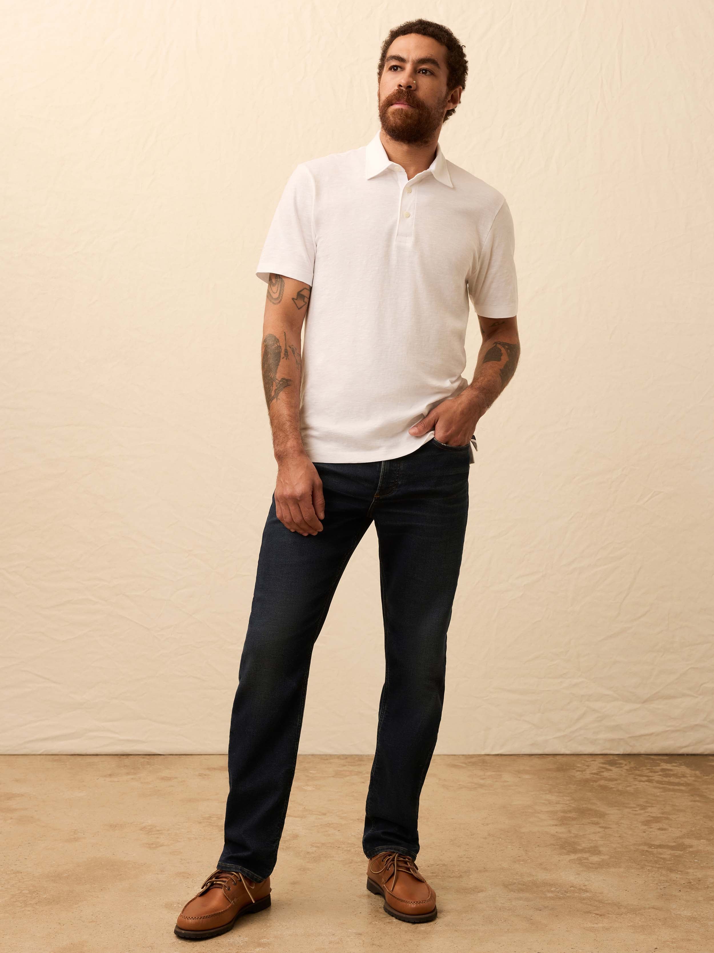 Man wearing a white polo shirt and dark jeans against a beige background