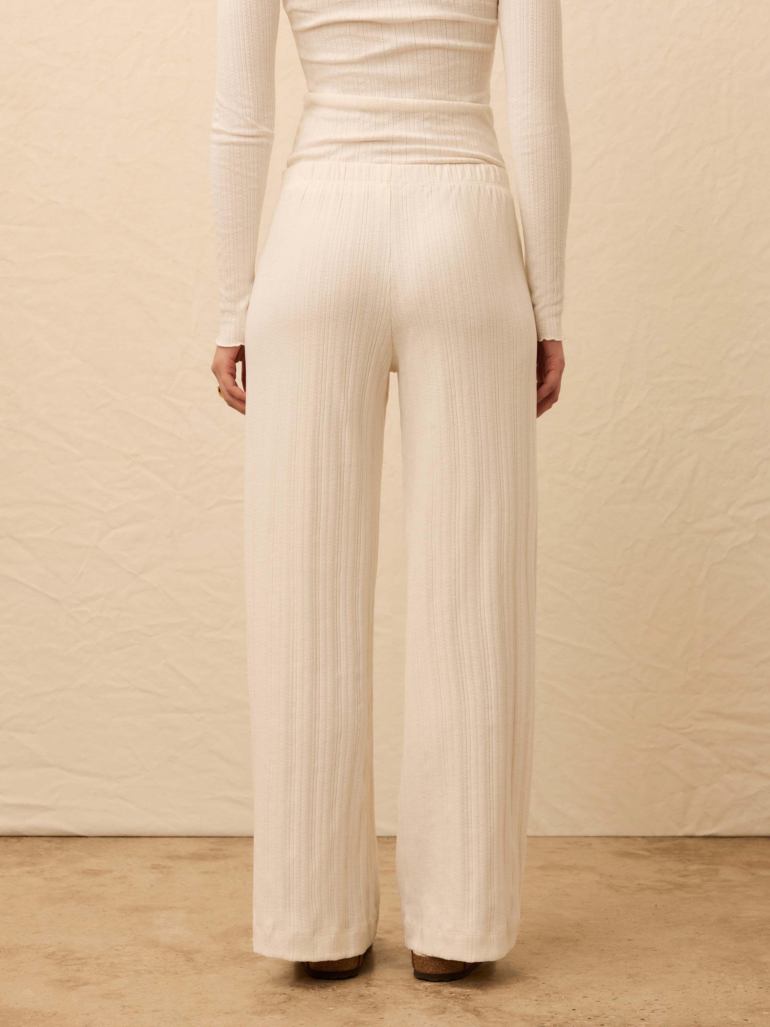 Woman wearing a white top with matching pants against a beige background