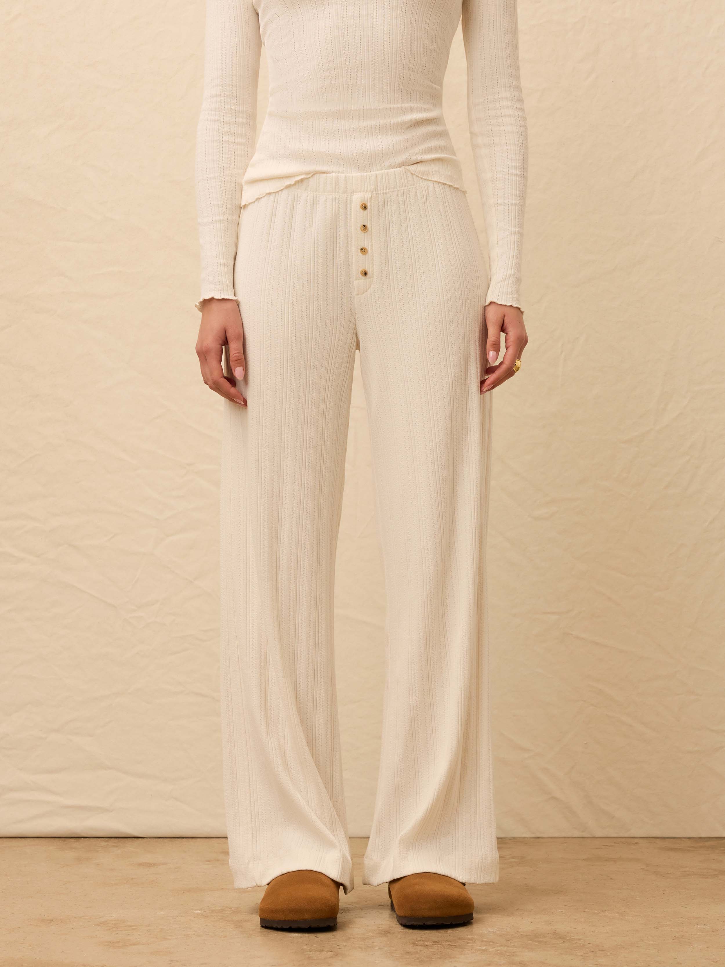 Woman wearing a white top with matching pants against a beige background
