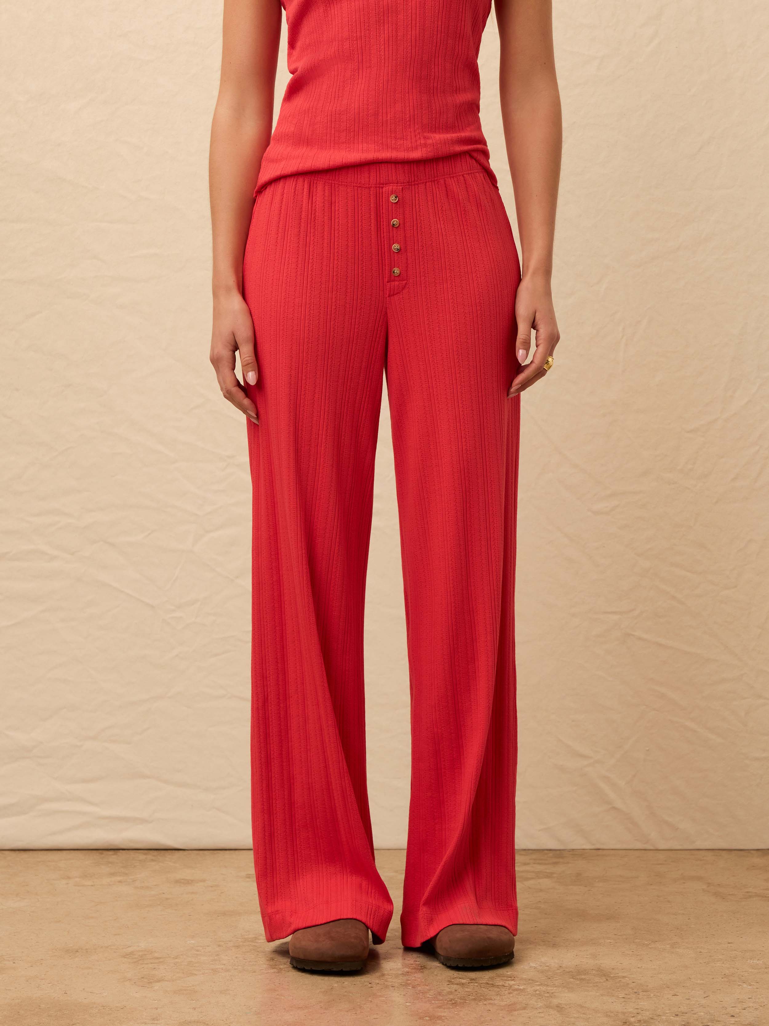 Woman wearing red tank and matching pant against beige background