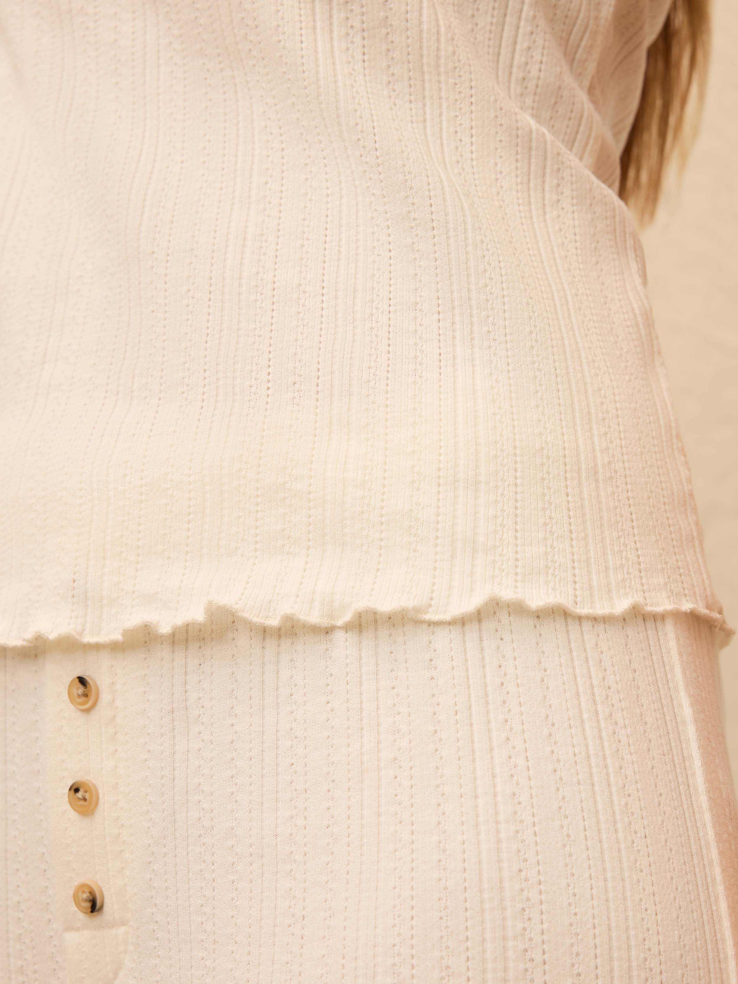 Closeup of a ribbed white tank top and matching pants with button detail
