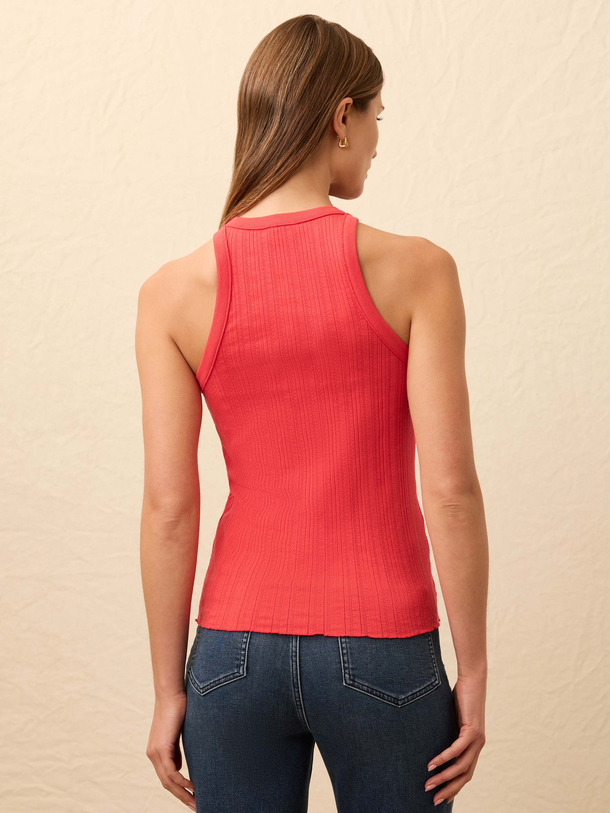Woman wearing red tank and jeans against a beige background
