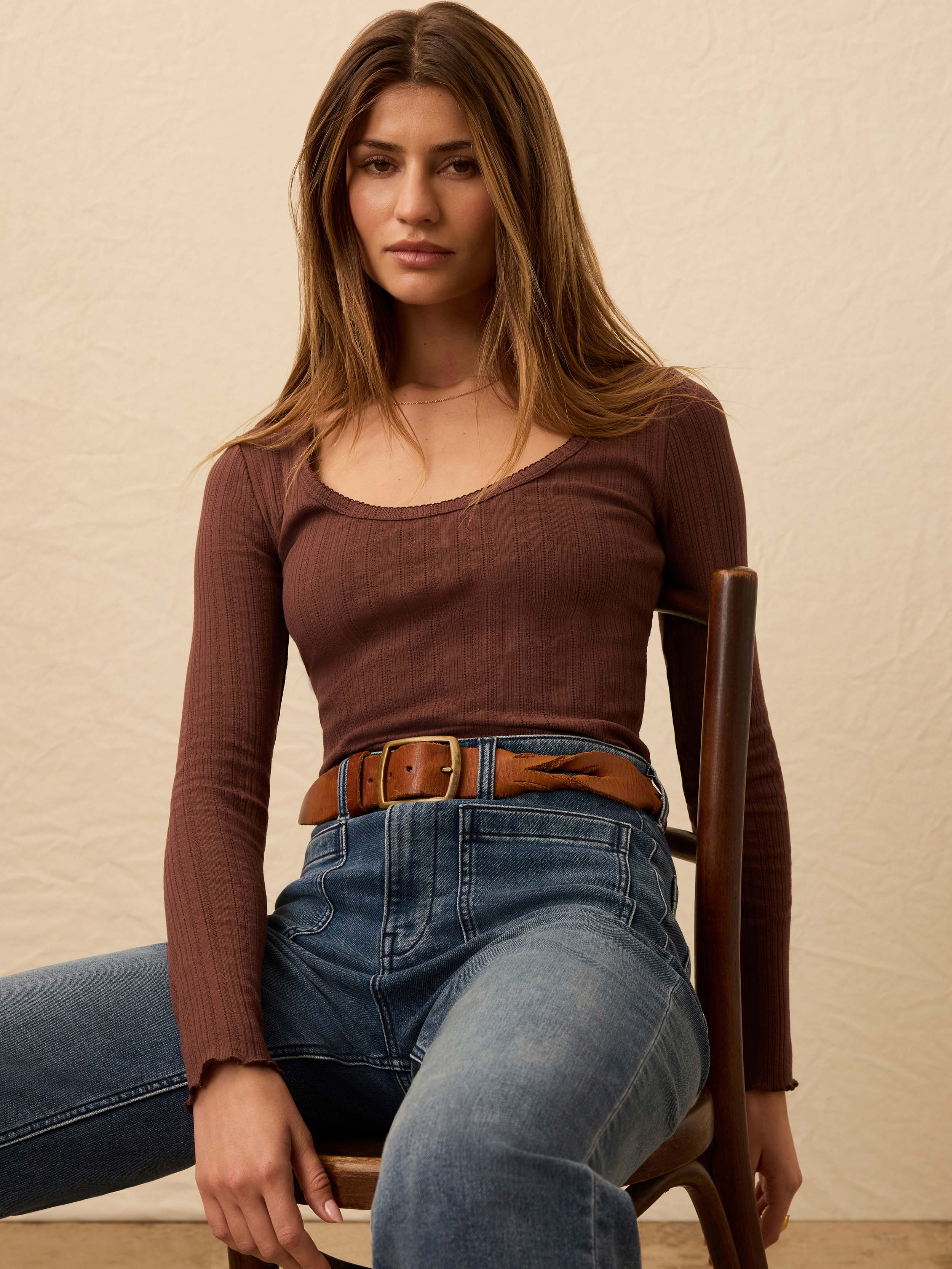 Woman wearing a brown long sleeve ribbed shirt with jeans against a beige background