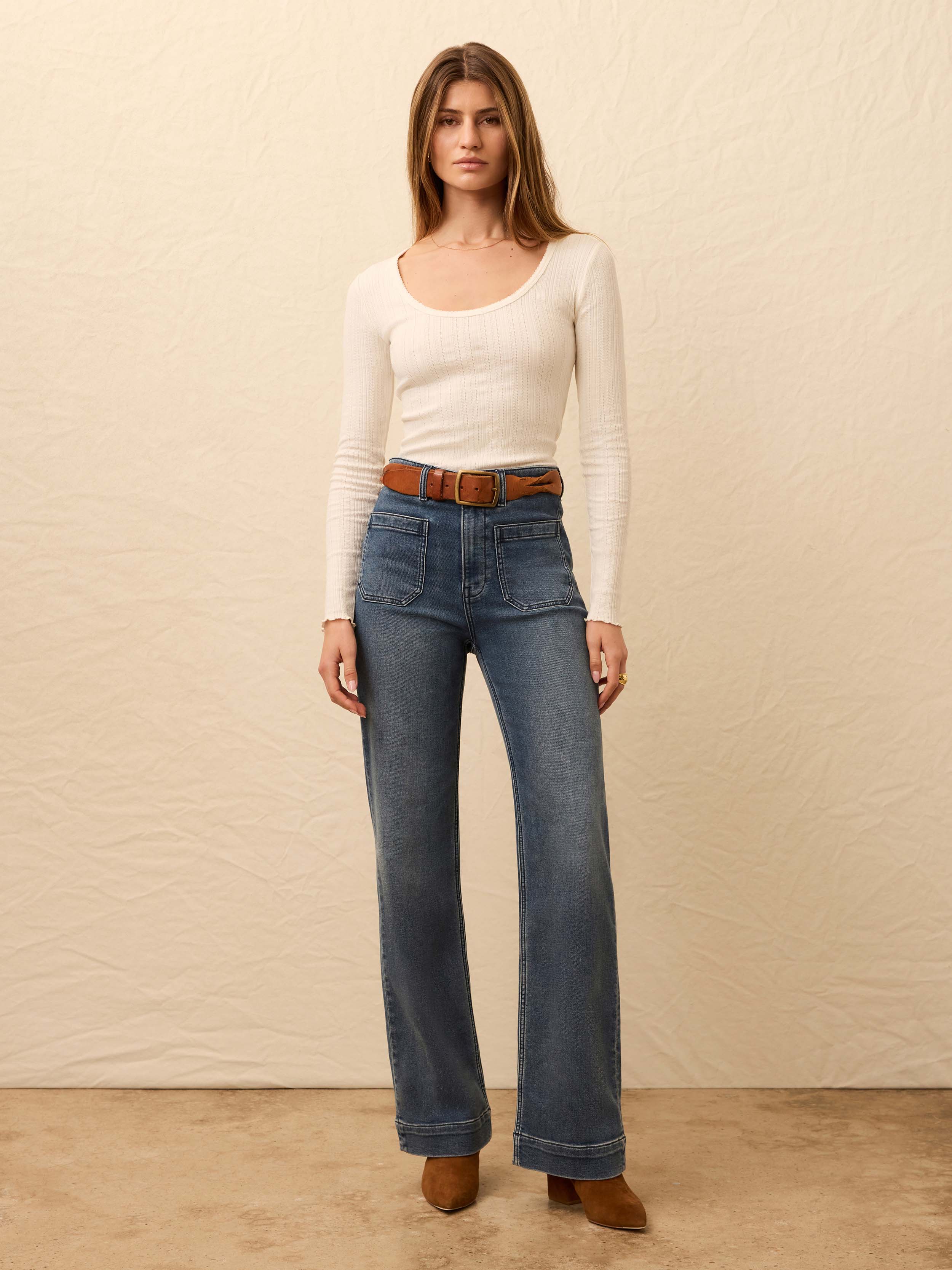 Woman wearing a white ribbed long sleeve shirt and jeans against a beige background