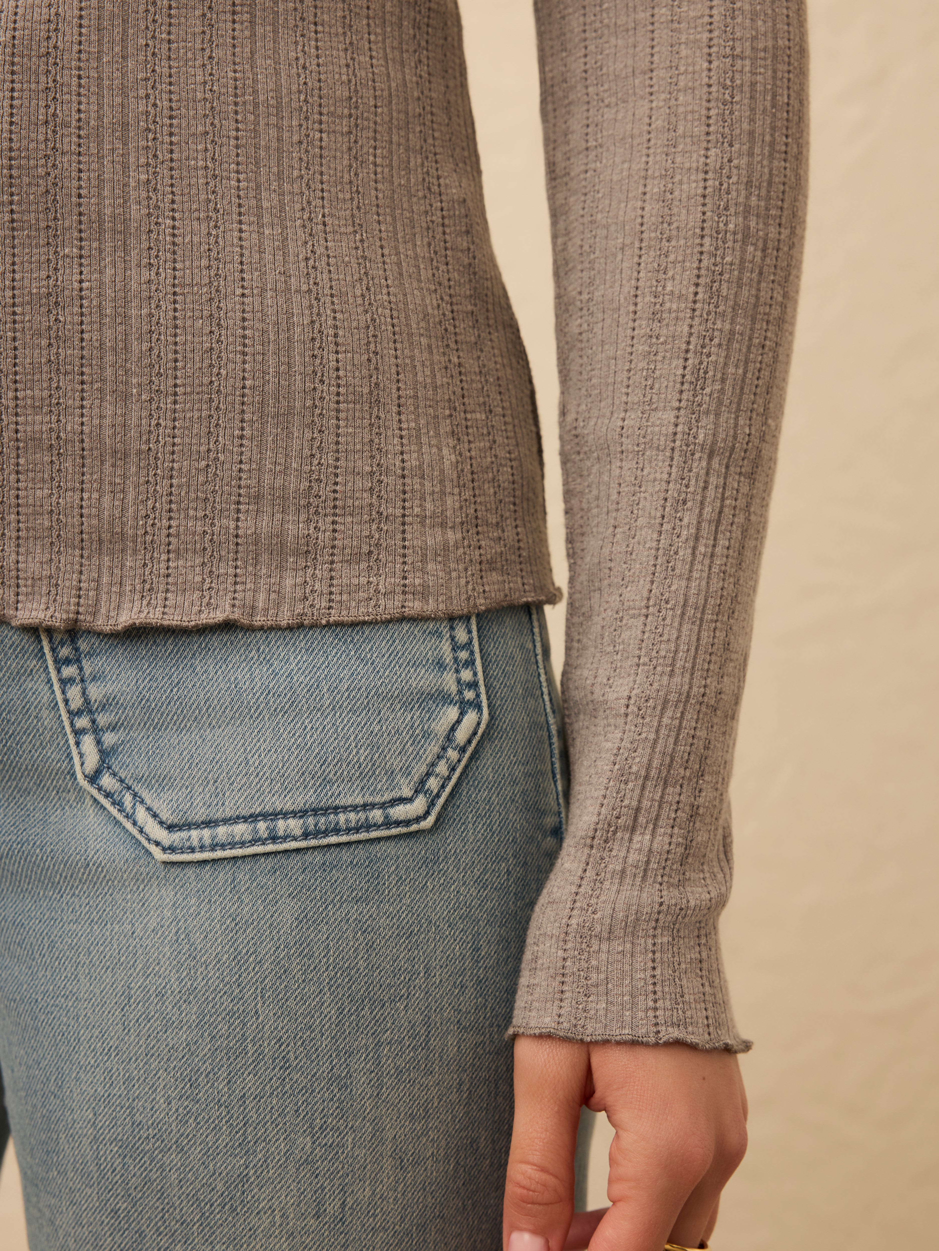 Close up of grey long sleeve ribbed top against a beige background