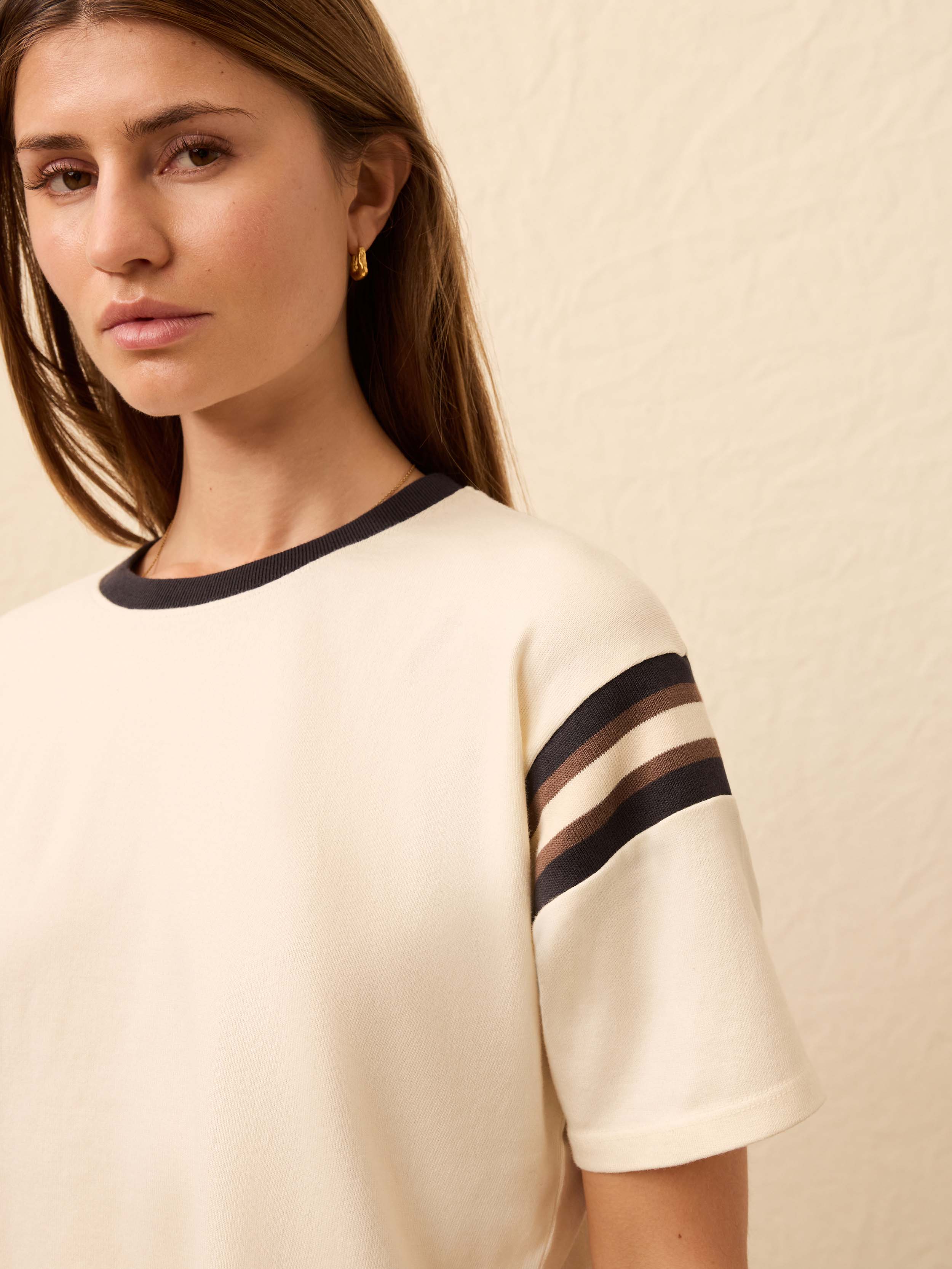 Woman is wearing a white jersey tee against a beige background