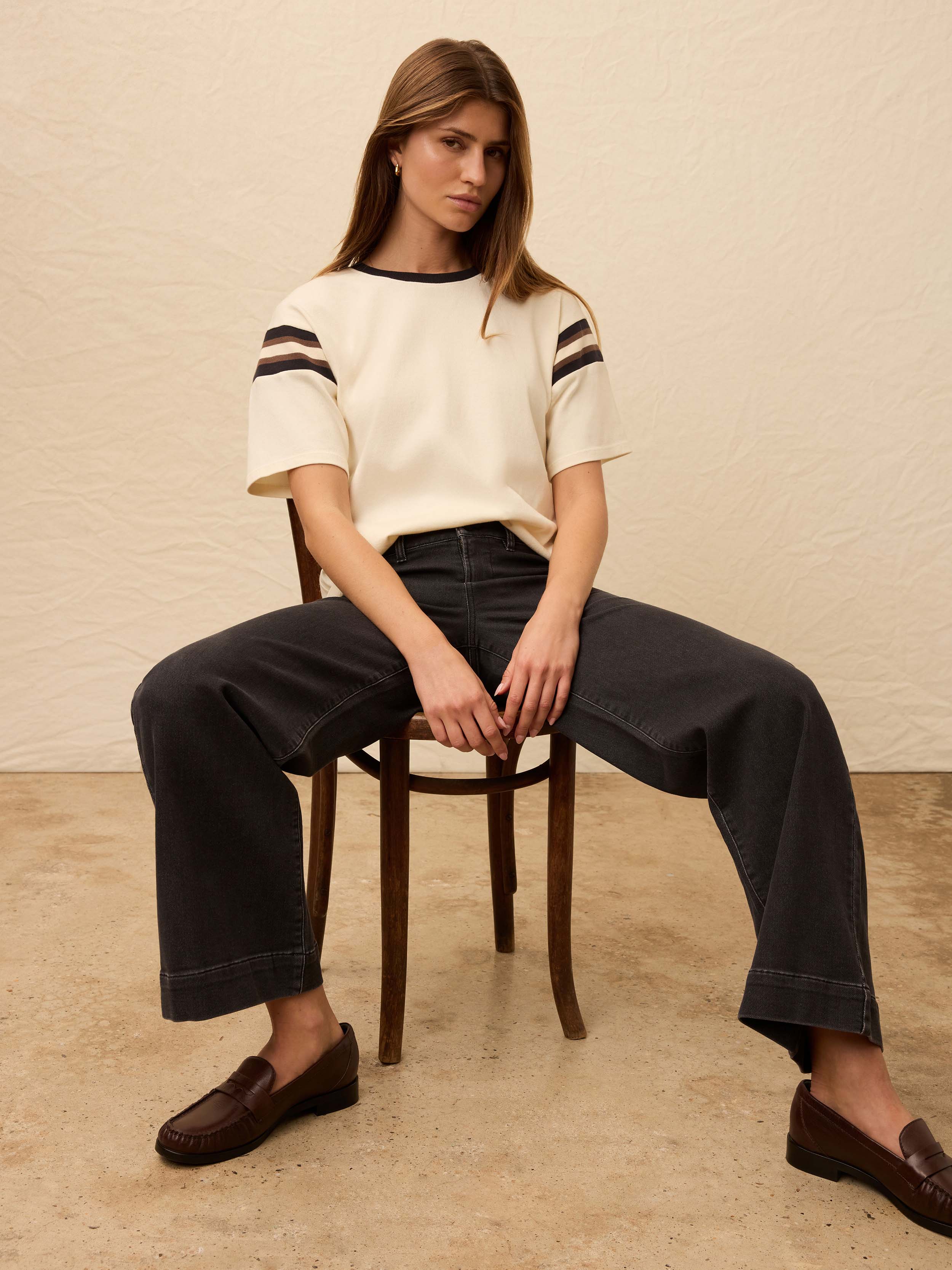 Woman is wearing a white sport jersey tee with black jeans against a beige background